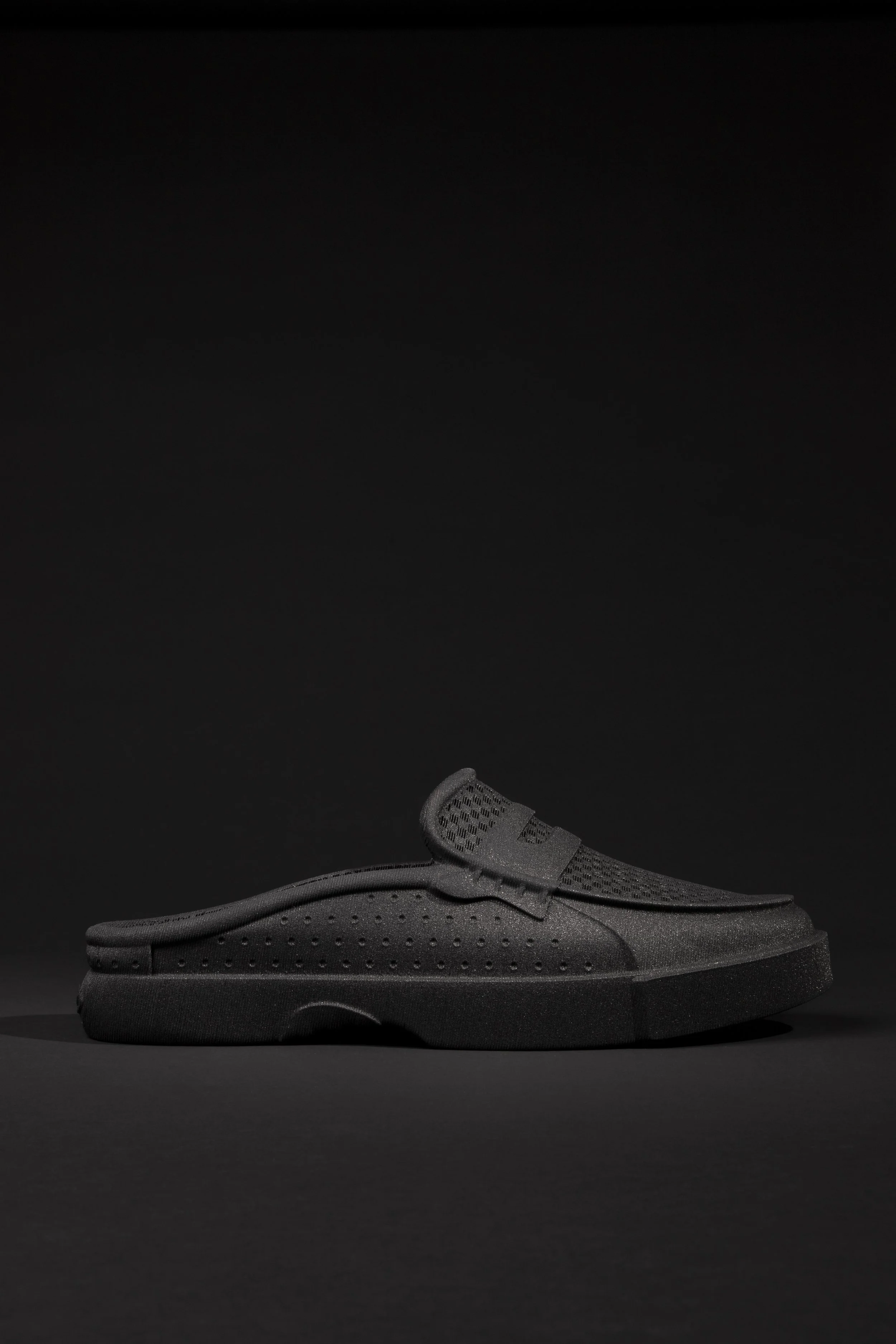Black athletic sneaker with perforated design on a black background.
