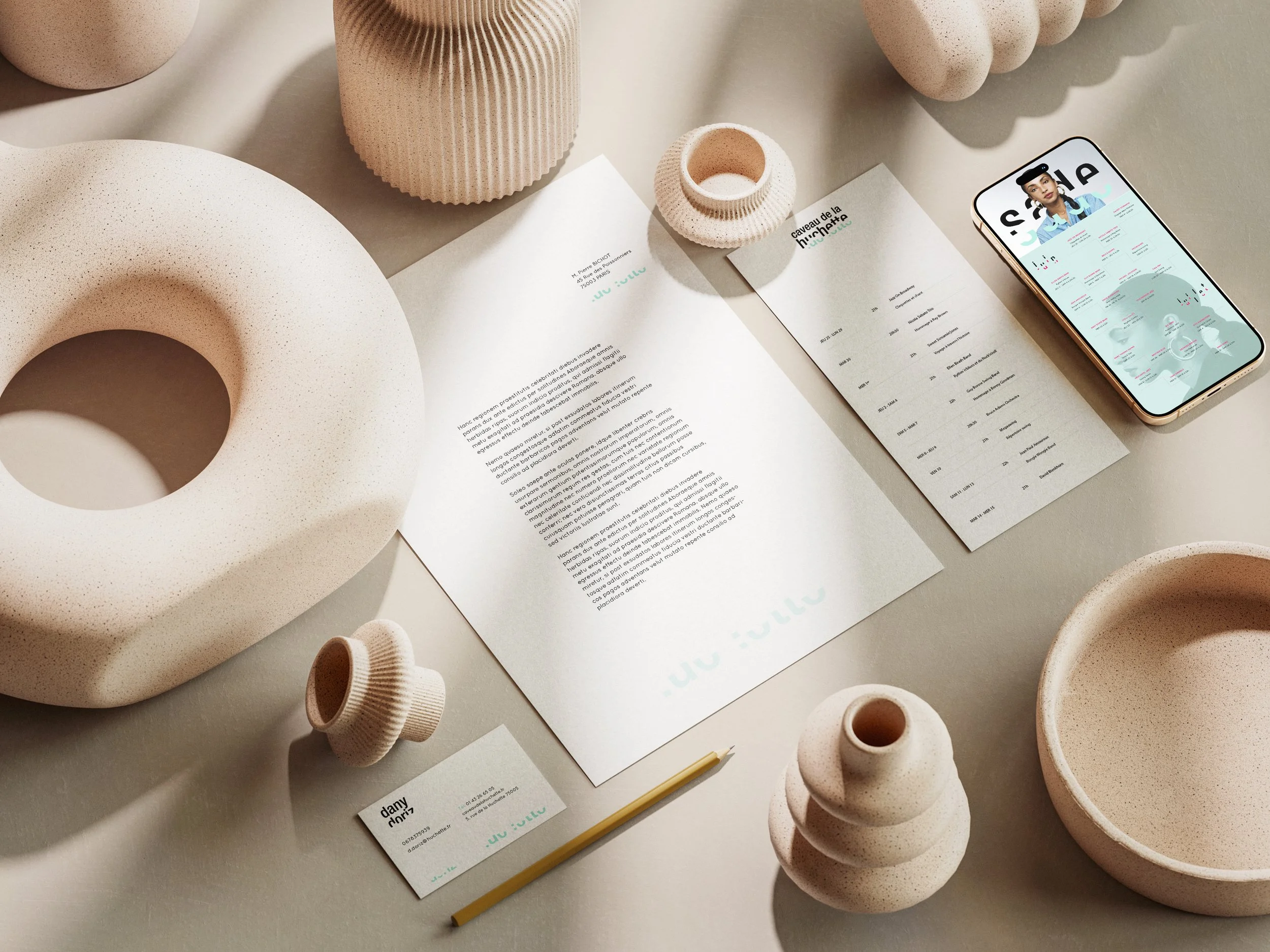 Arrangement of beige textured ceramic vases and bowls with some overlapping, next to a sheet of paper with text and a business card, on a light-colored surface.