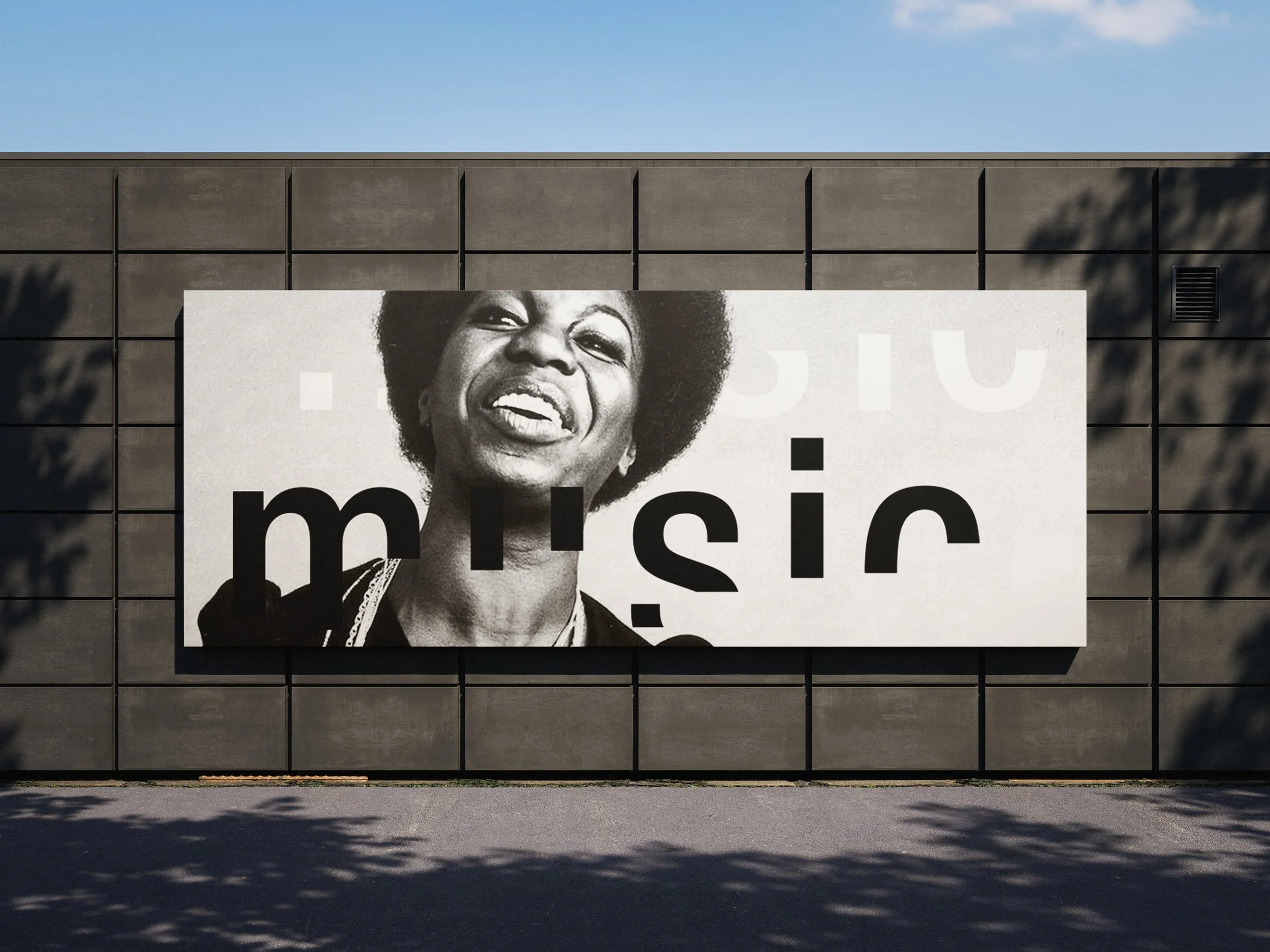 Large black-and-white poster of a woman smiling, mounted on a wall with shadows from trees.