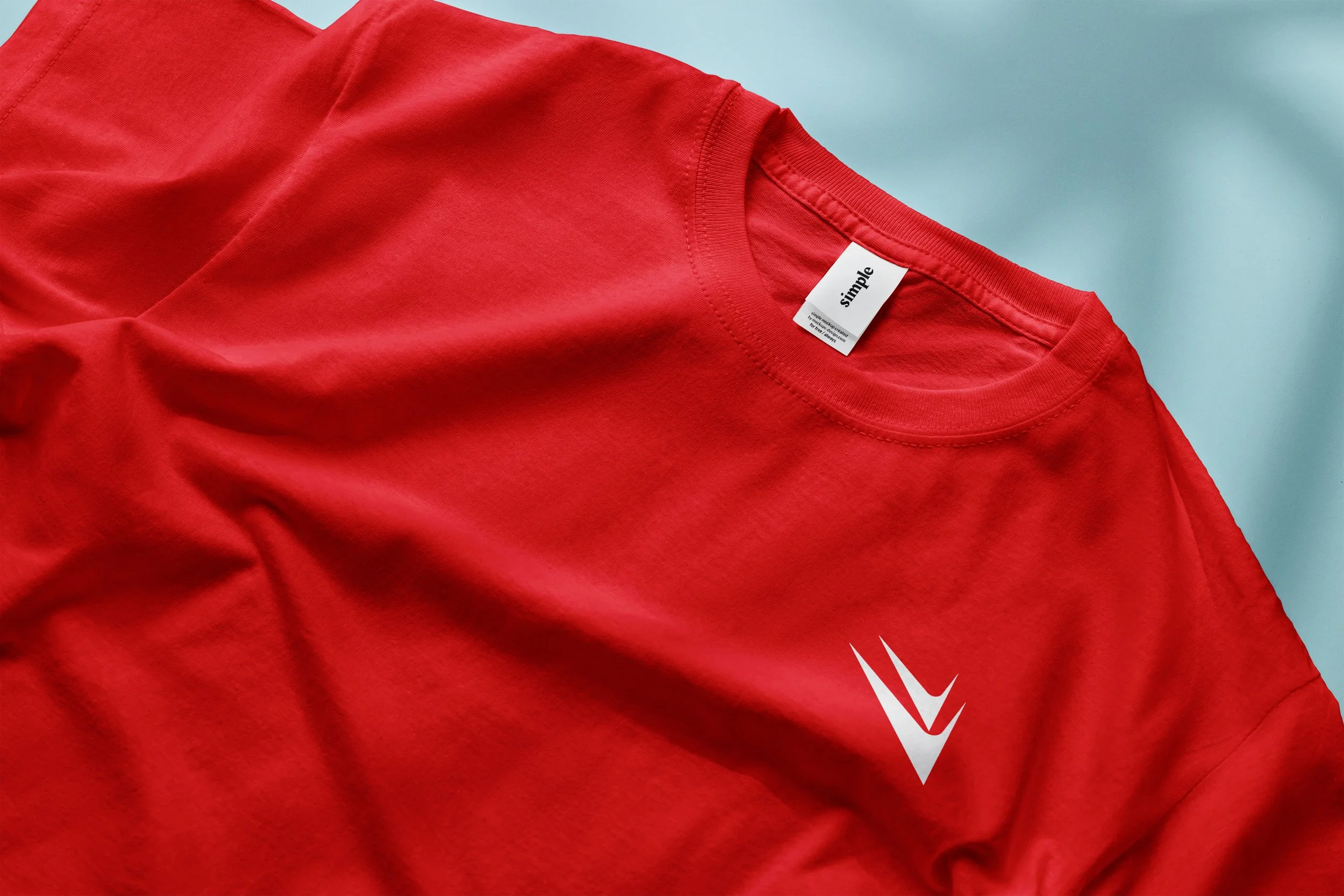 Close-up of a red T-shirt with a white tag that has the word 'simple' on it, and a small white graphic design on the lower part of the shirt.
