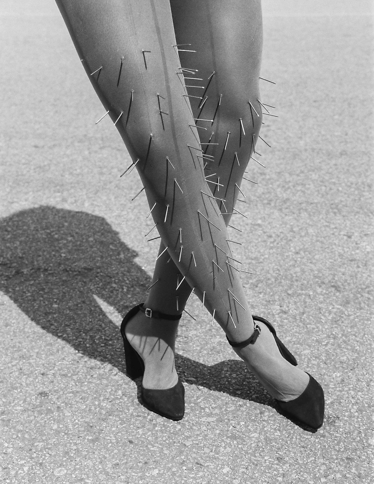 crossed legs of a woman standing wearing tights with nails pierced on it