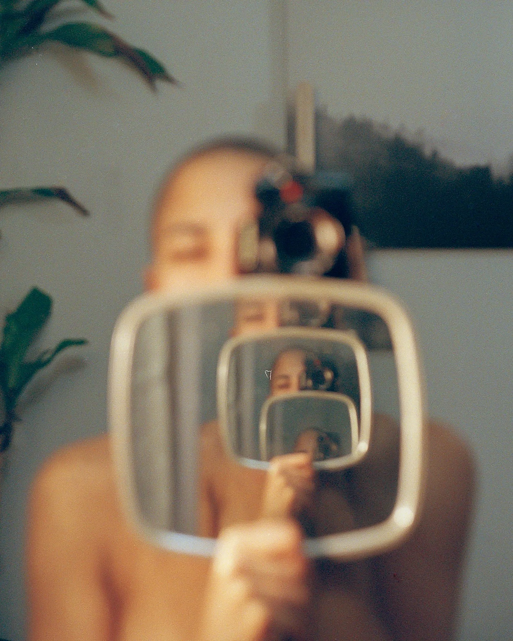 a photographer taking a photograph of themself using a handheld mirror and large mirror creating a multiplication of themself in the mirrors