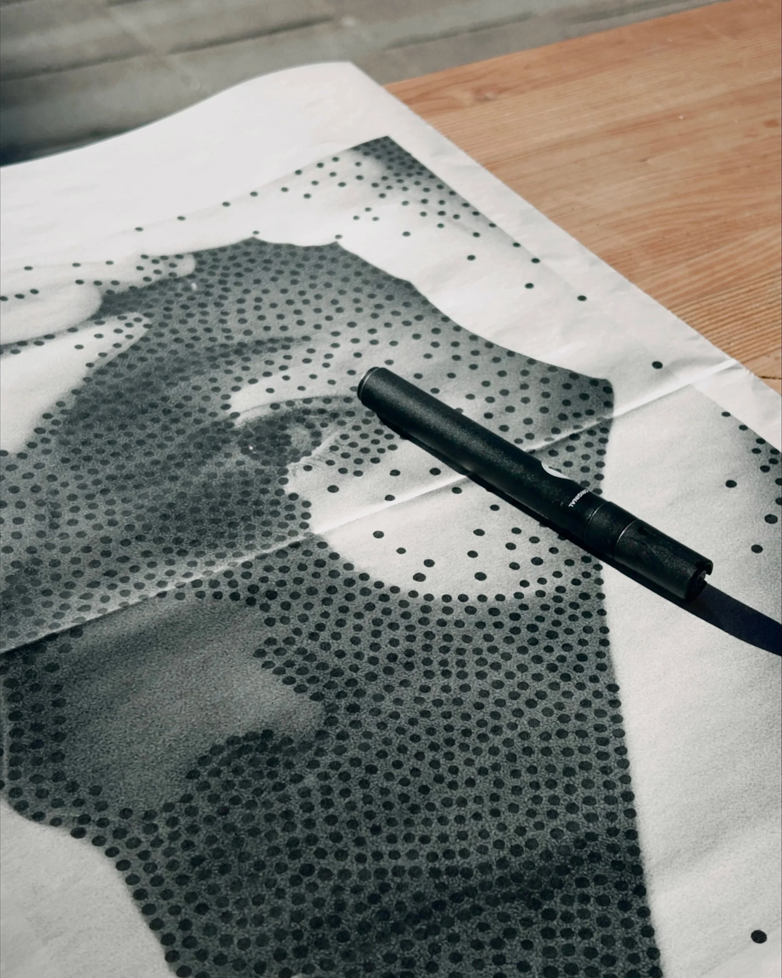 Close-up of a newsprint paper with black polka dots partially covered by a black marker pen, on a wooden surface.