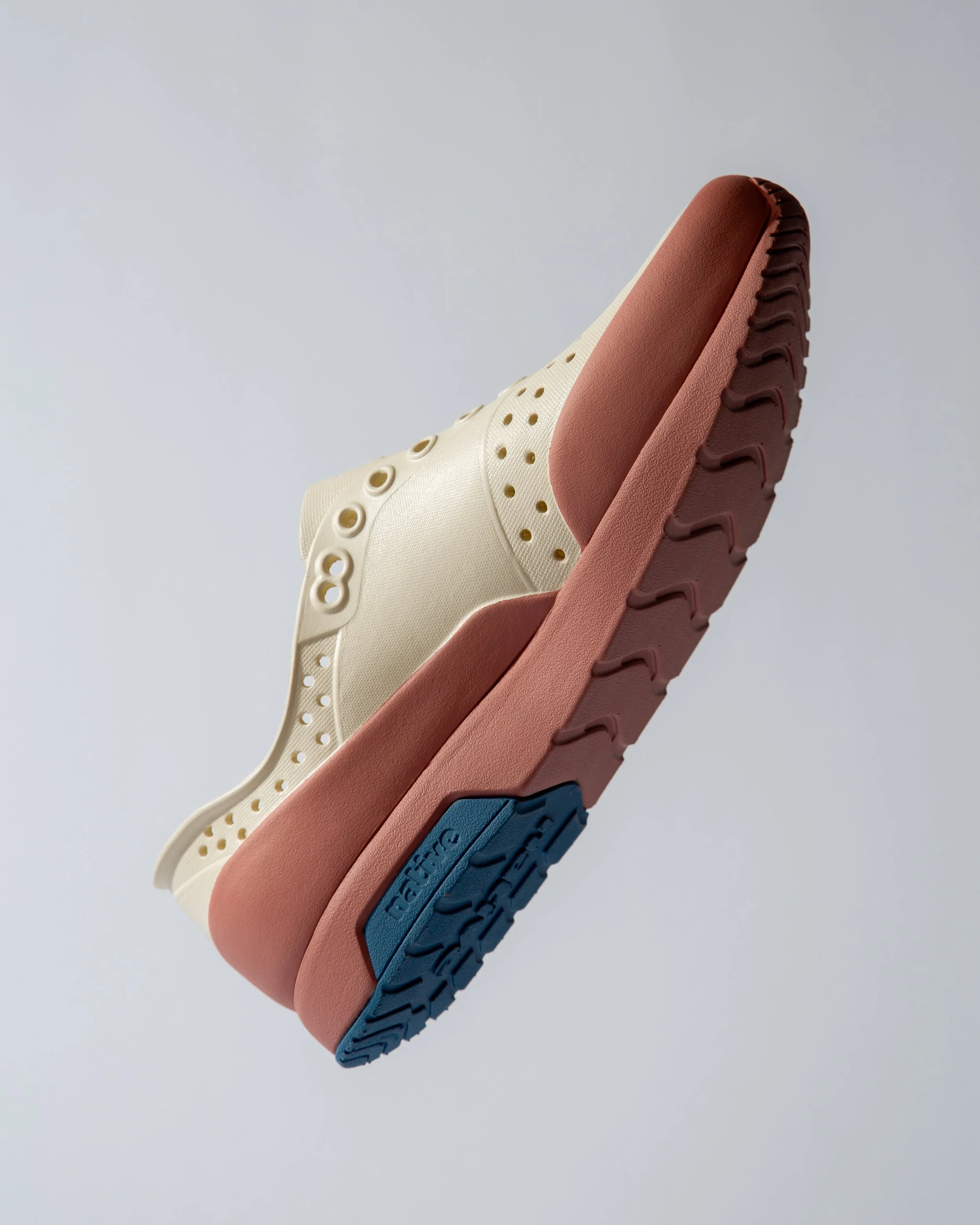 Close-up of four different colored sneakers stacked with the soles facing up, showing various tread patterns and textures.