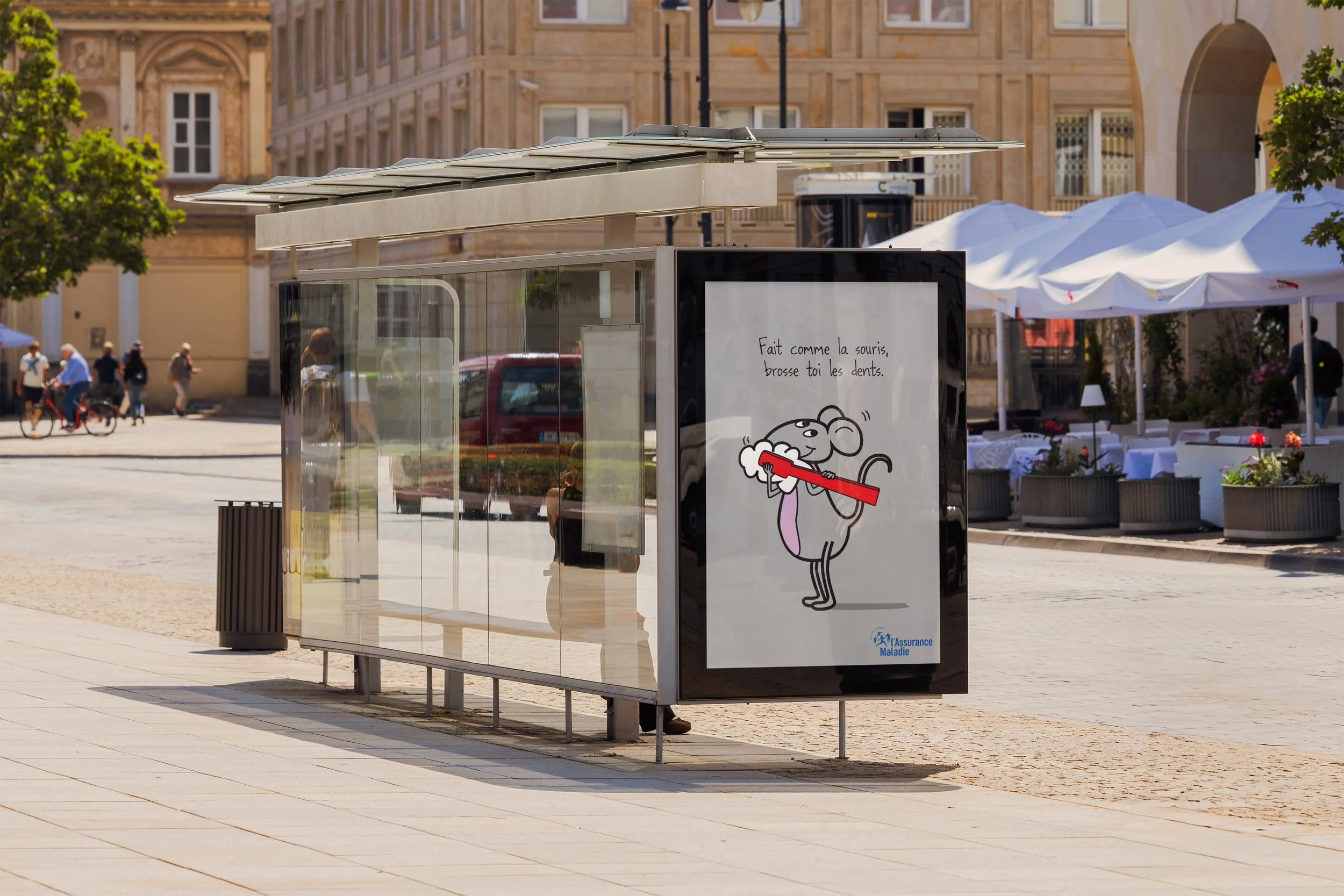 A bus stop shelter in an urban square with drawn mouse illustration holding a toothbrush and French text promoting dental hygiene. The background features historic buildings, trees, and outdoor seating areas with white umbrellas.