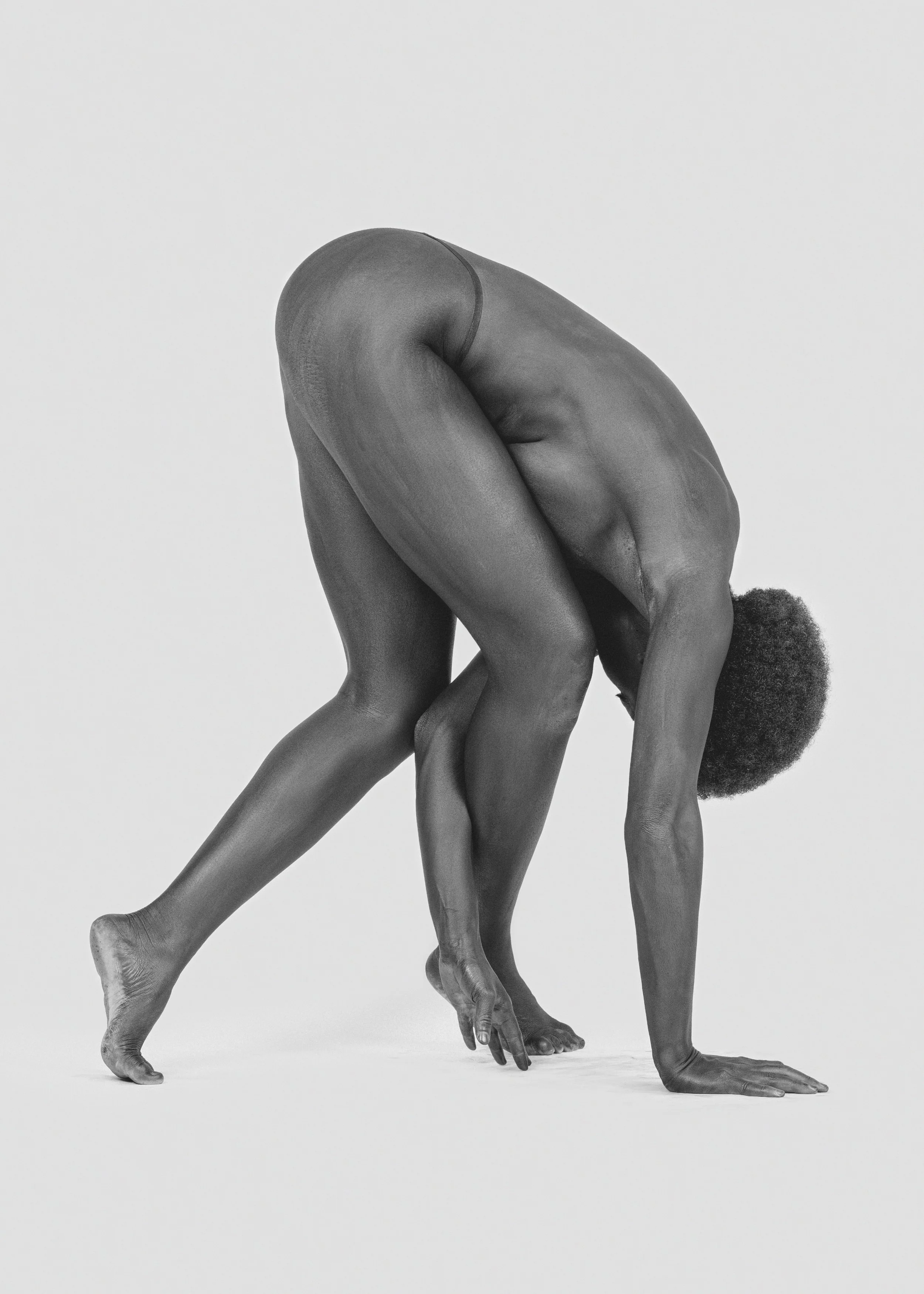 Black and white photograph of a nude person in a yoga pose, with hands and feet on the ground and body arched.