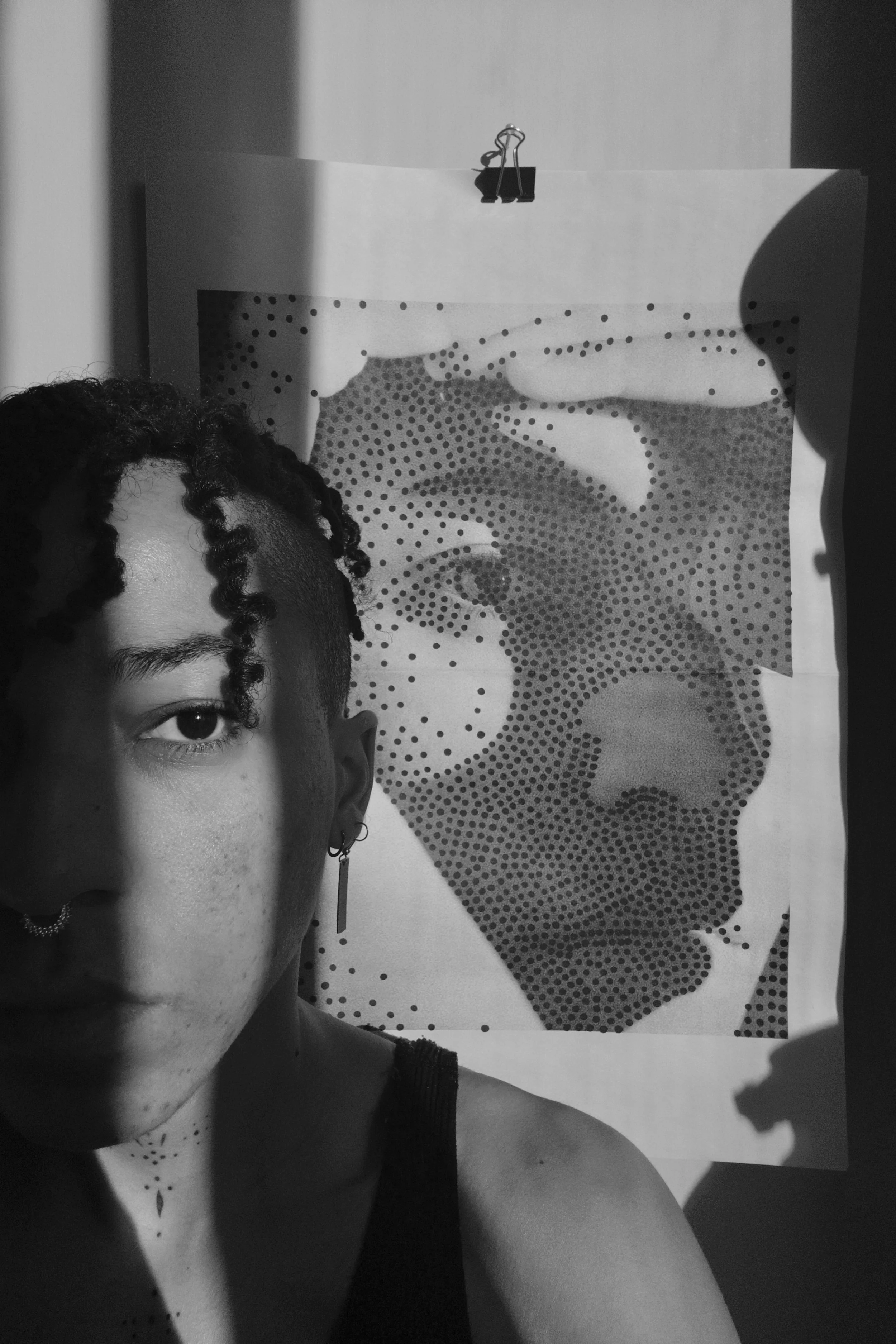 photograph of and image nailed to the wall of a portrait with dots on it, with a woman next to the image look away from it