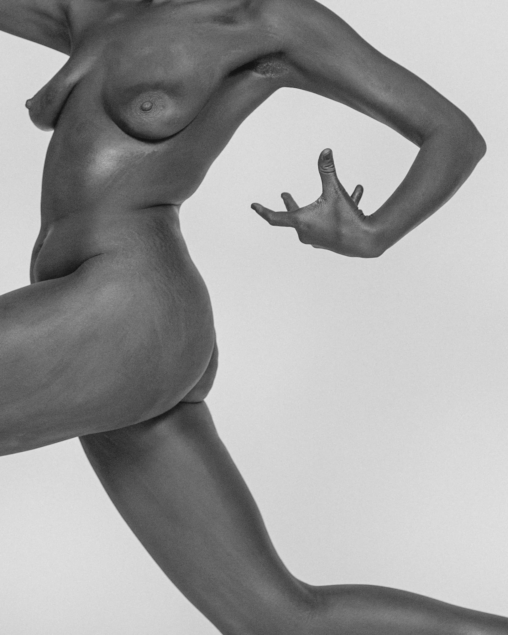A close-up black and white photograph of a person's torso and arm. The person is posed with one hand on their hip and the other arm bent, with fingers in a relaxed position. The image emphasizes the contours and musculature of the body.