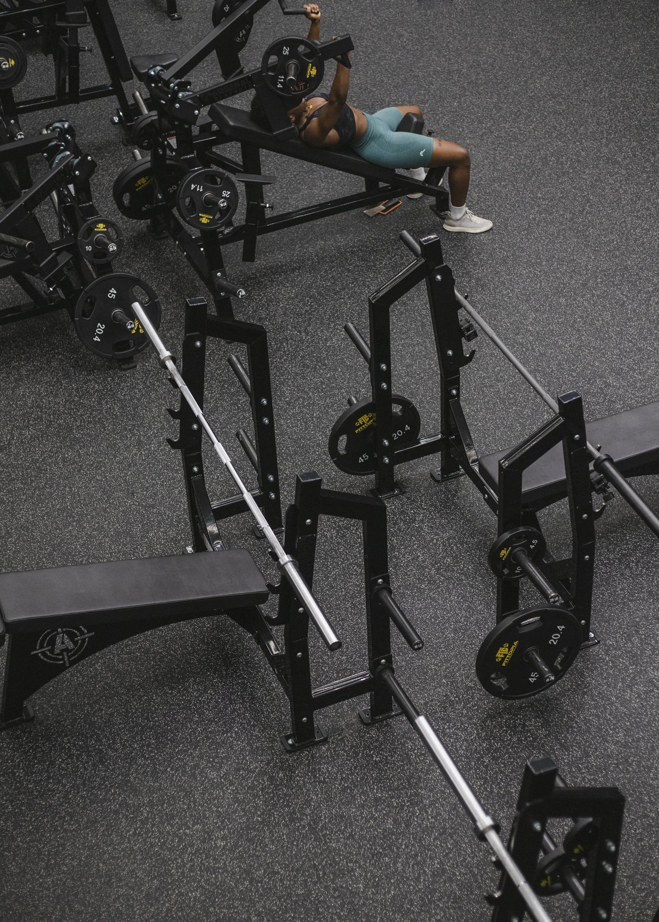 A woman lying on a workout bench in a gym, lifting weights with a barbell.