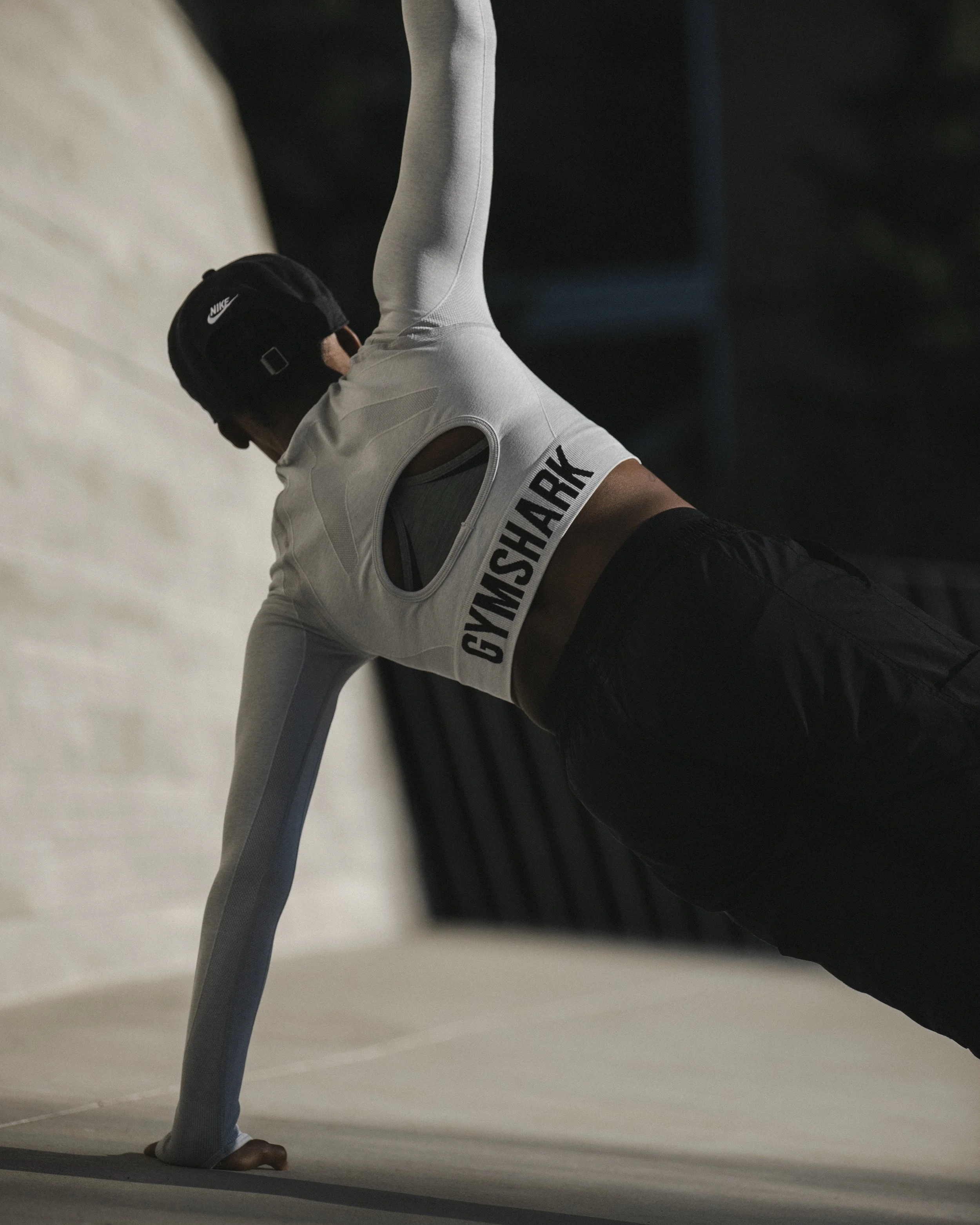 A person doing yoga on a mat, wearing a Nike cap, sports bra, and leggings, extending one arm upward and looking down.