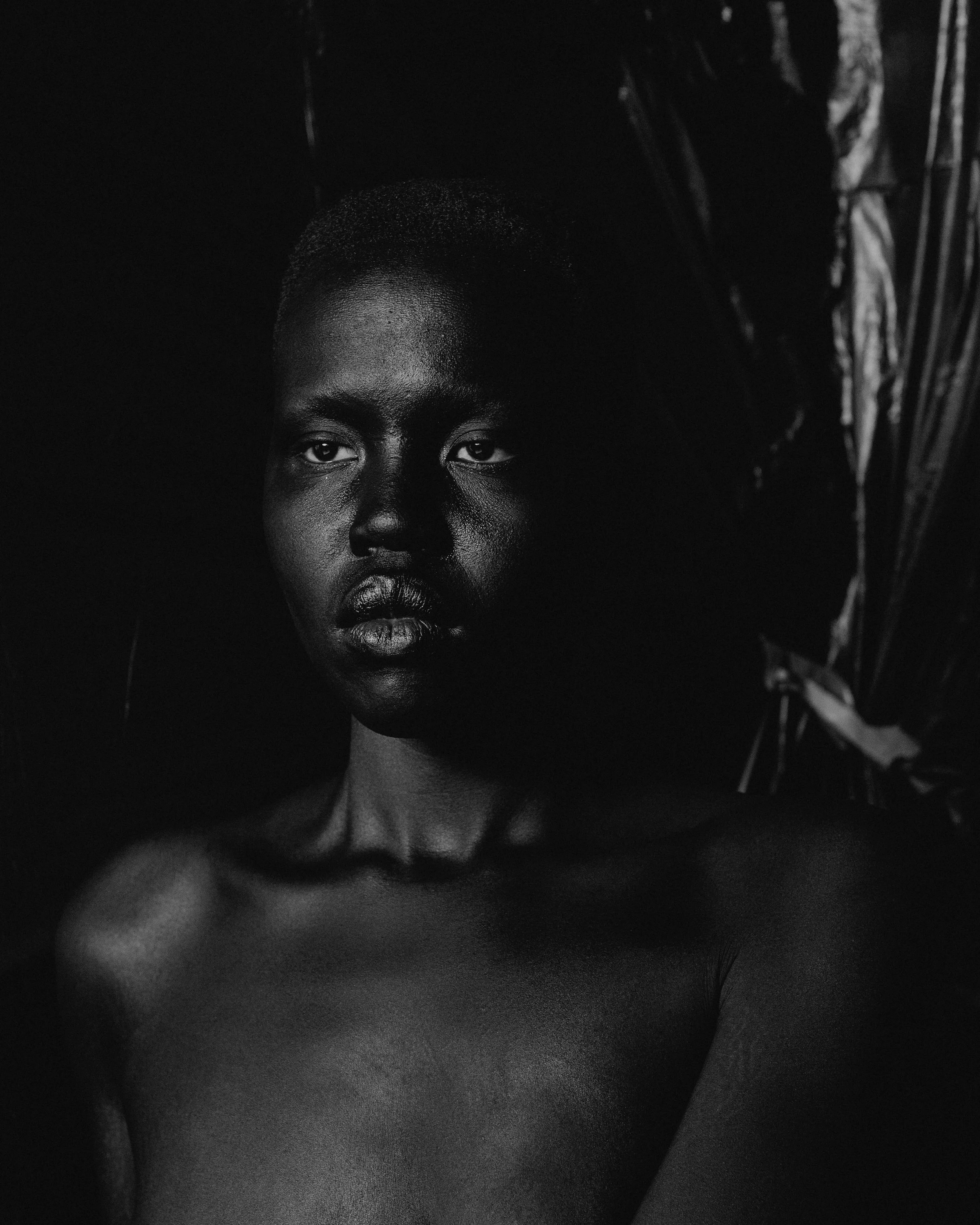 A dark black and white portrait of a black woman, appearing to be nude looking away with sleepy eyes