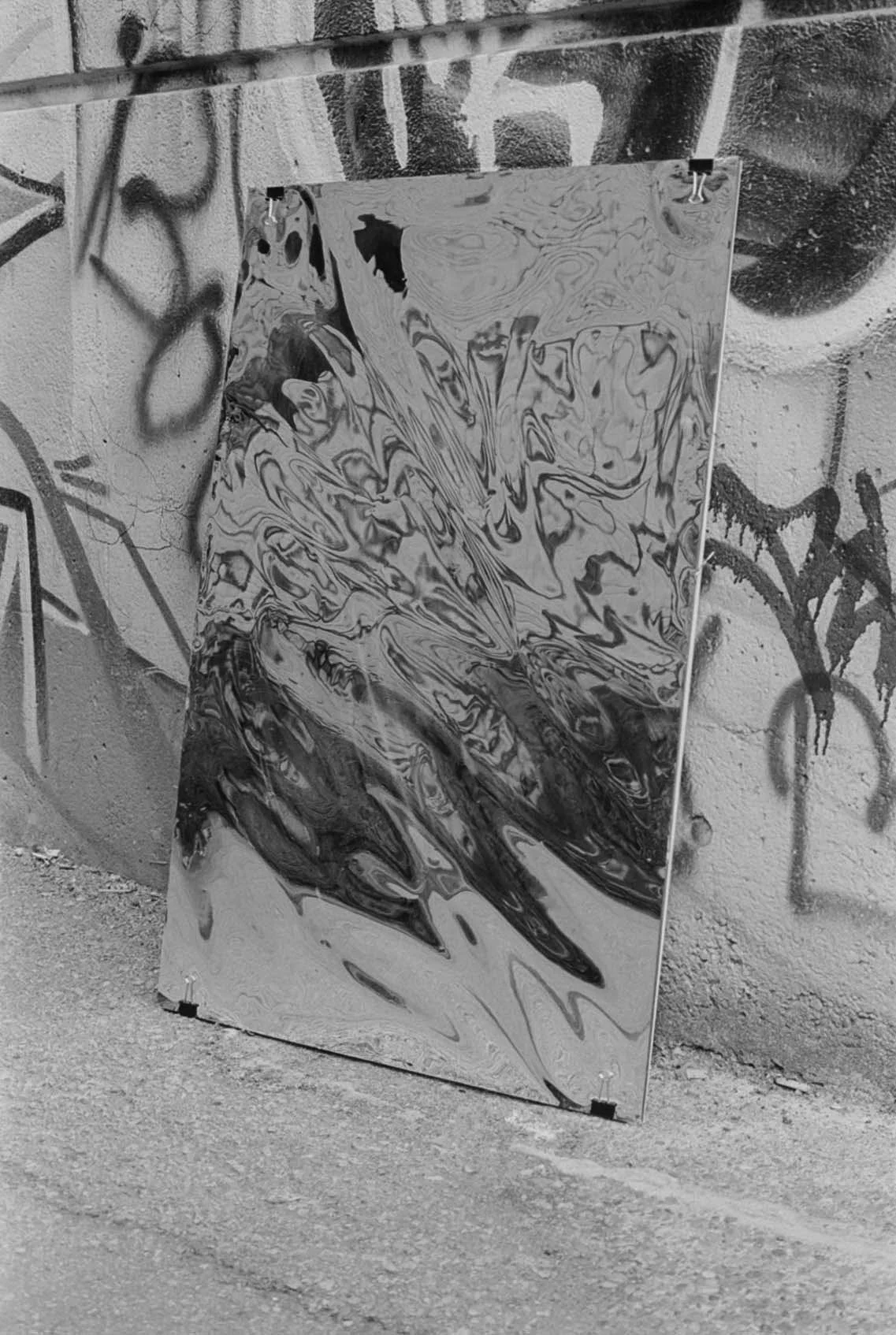 A marble-patterned abstract painting leaning against a graffiti-covered brick wall. The painting features swirling black and white patterns.