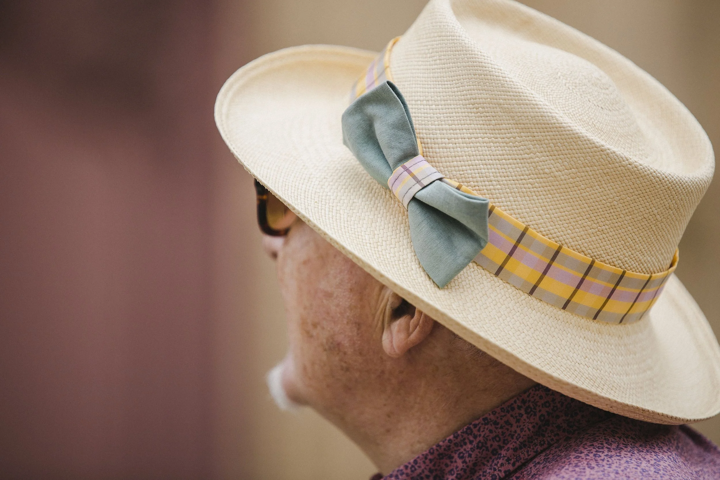 A woman wearing a white sunhat with a colorful plaid ribbon and a blue bow, and sunglasses.