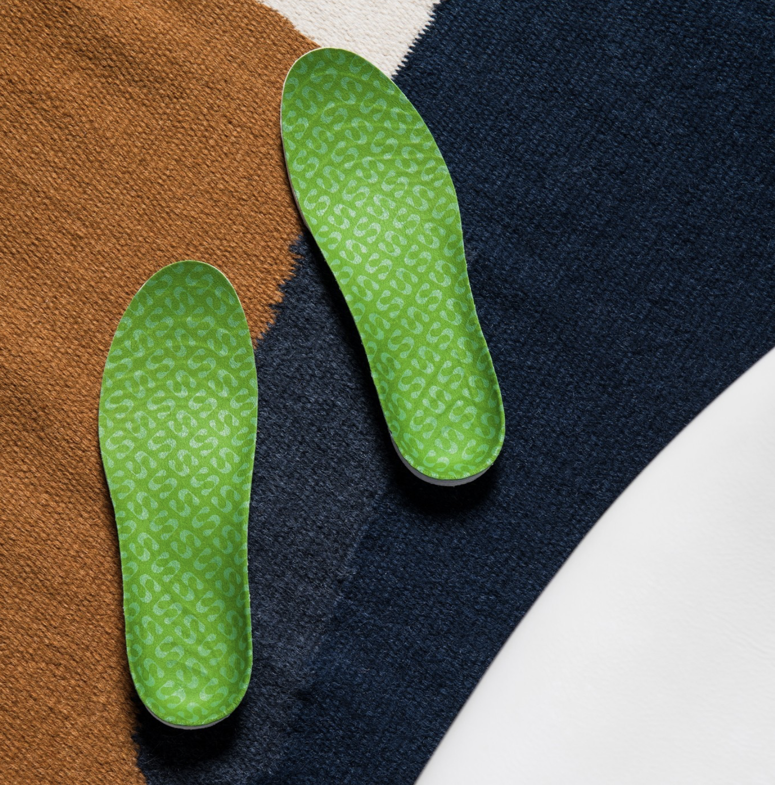 Close-up of two green insoles with a leopard print pattern on multi-colored textured surfaces.