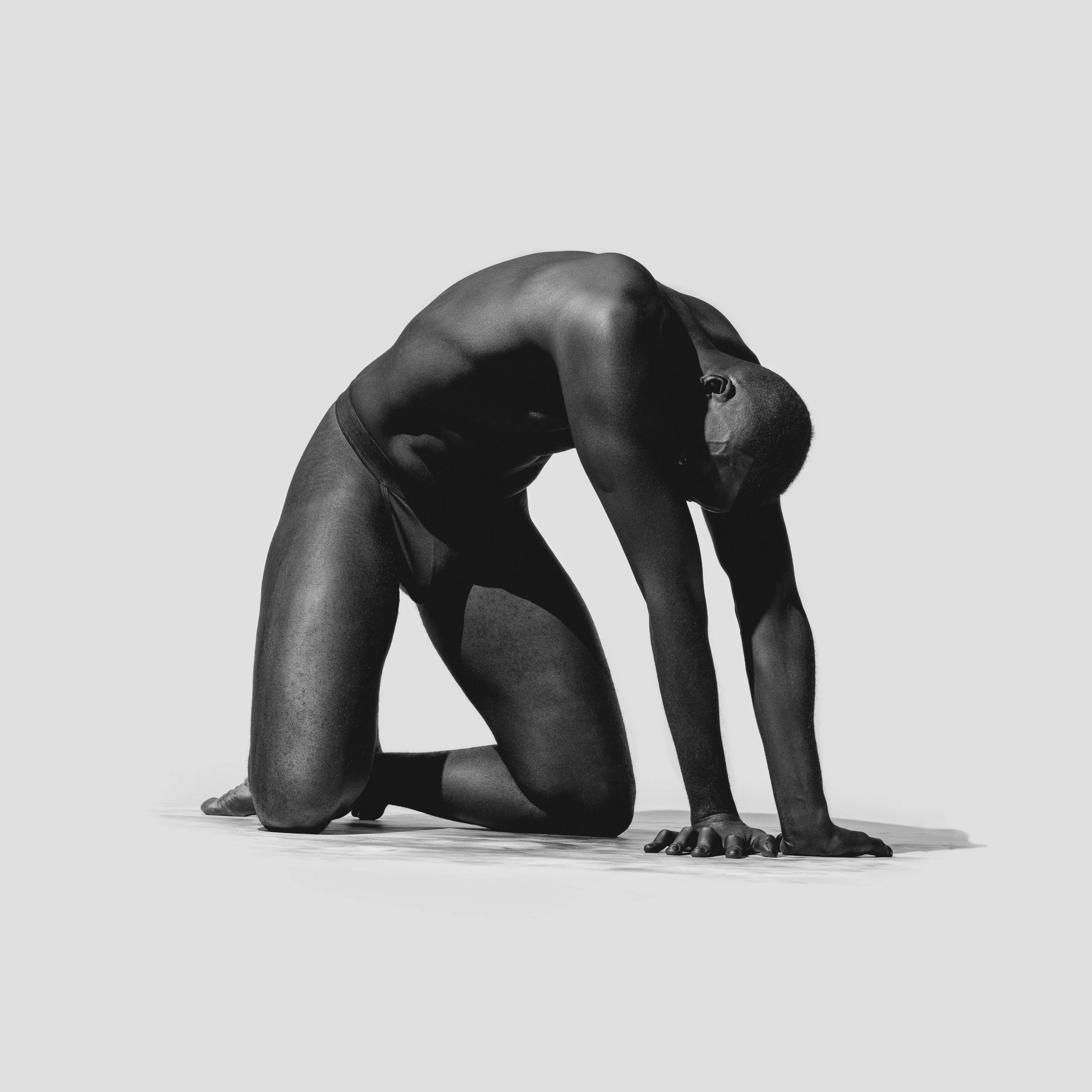 Black and white photograph of a person in a yoga pose, kneeling with head resting on the ground and arms stretched out forward
