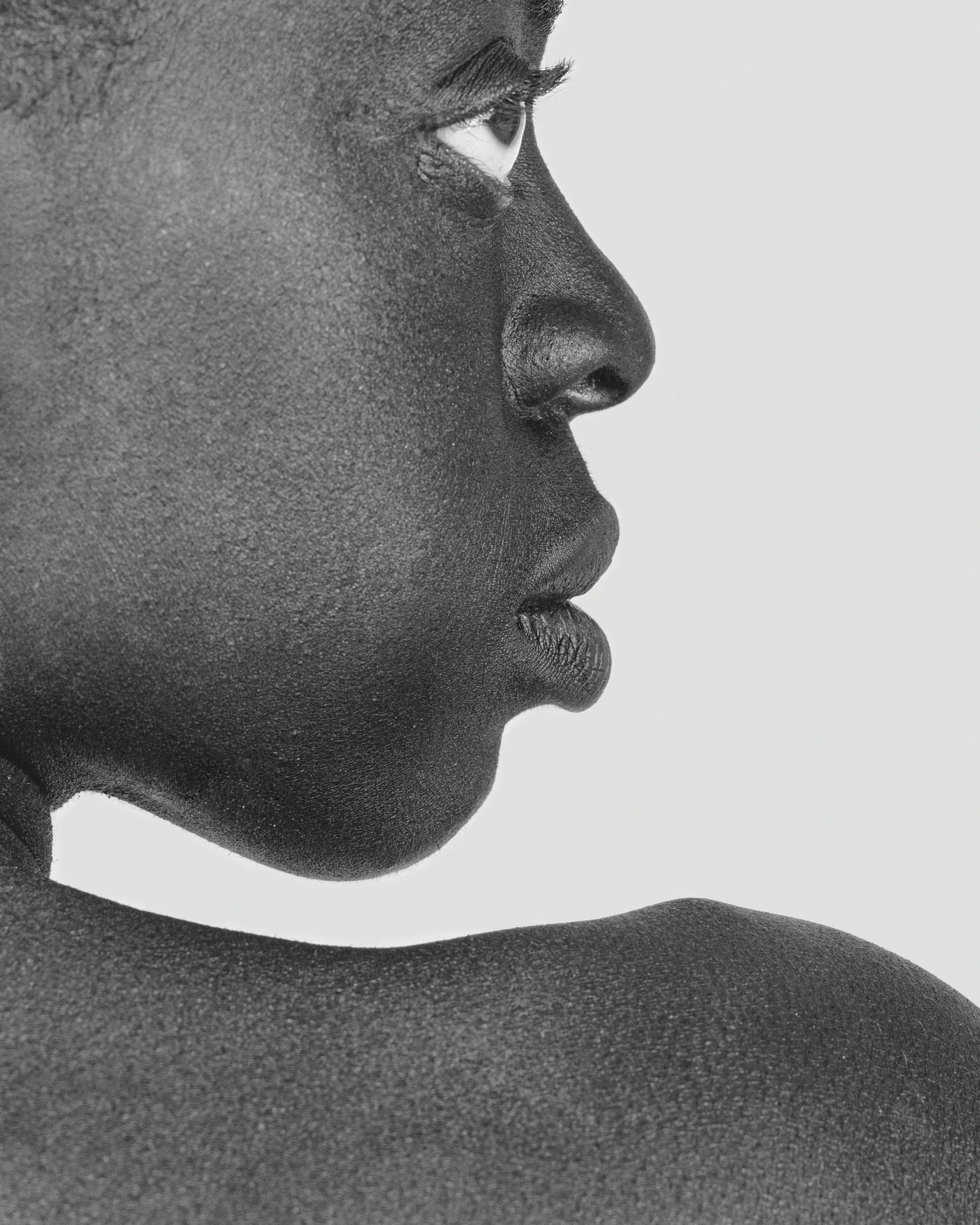 Close-up black and white photograph of a person's face in profile with textured skin, emphasizing the eye, nose, and lips.