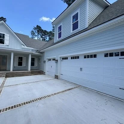View of a modern white house with a three-car garage, concrete driveway, and a front porch under a blue sky.