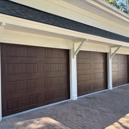 Three closed brown garage doors with white trim and brick driveway in front.