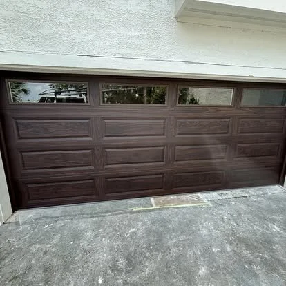 Closed brown garage door with rectangular panels and small windows at the top, on a concrete driveway.