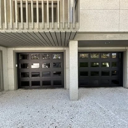 Two black garage doors side by side under a balcony on a concrete building.
