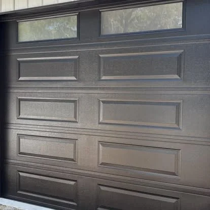 Close-up of a dark brown sectional garage door with four rectangular window panels at the top.