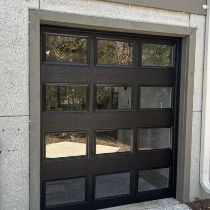 Modern black garage door with glass panels surrounded by a concrete frame.