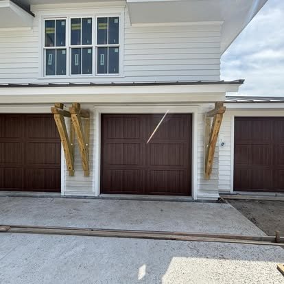 Garage with two brown doors under a white house, wooden supports on either side of the left door, and a small window above.