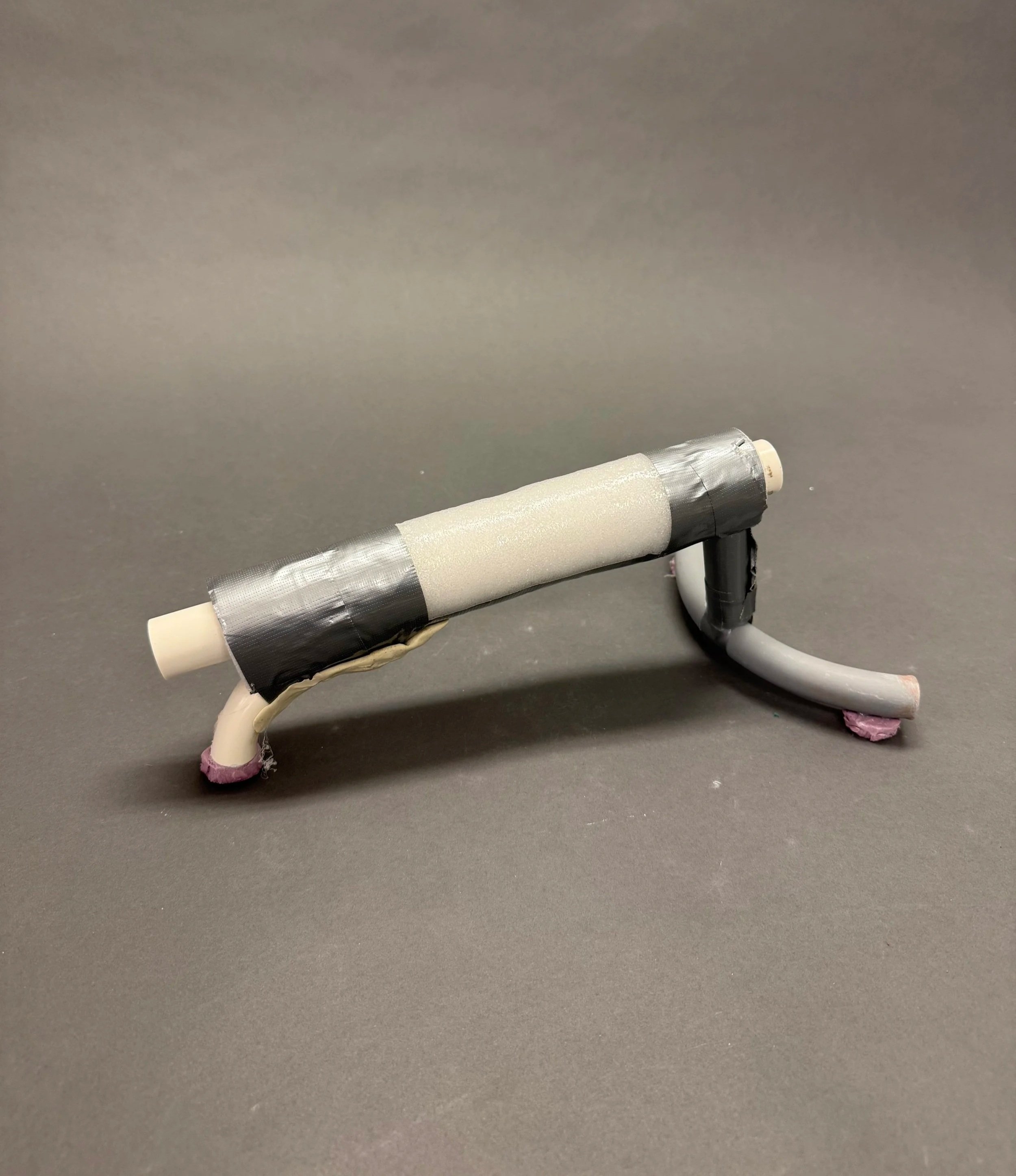 A homemade toy rocket made from cardboard tubes, duct tape, and paper, positioned on a black surface against a gray background.