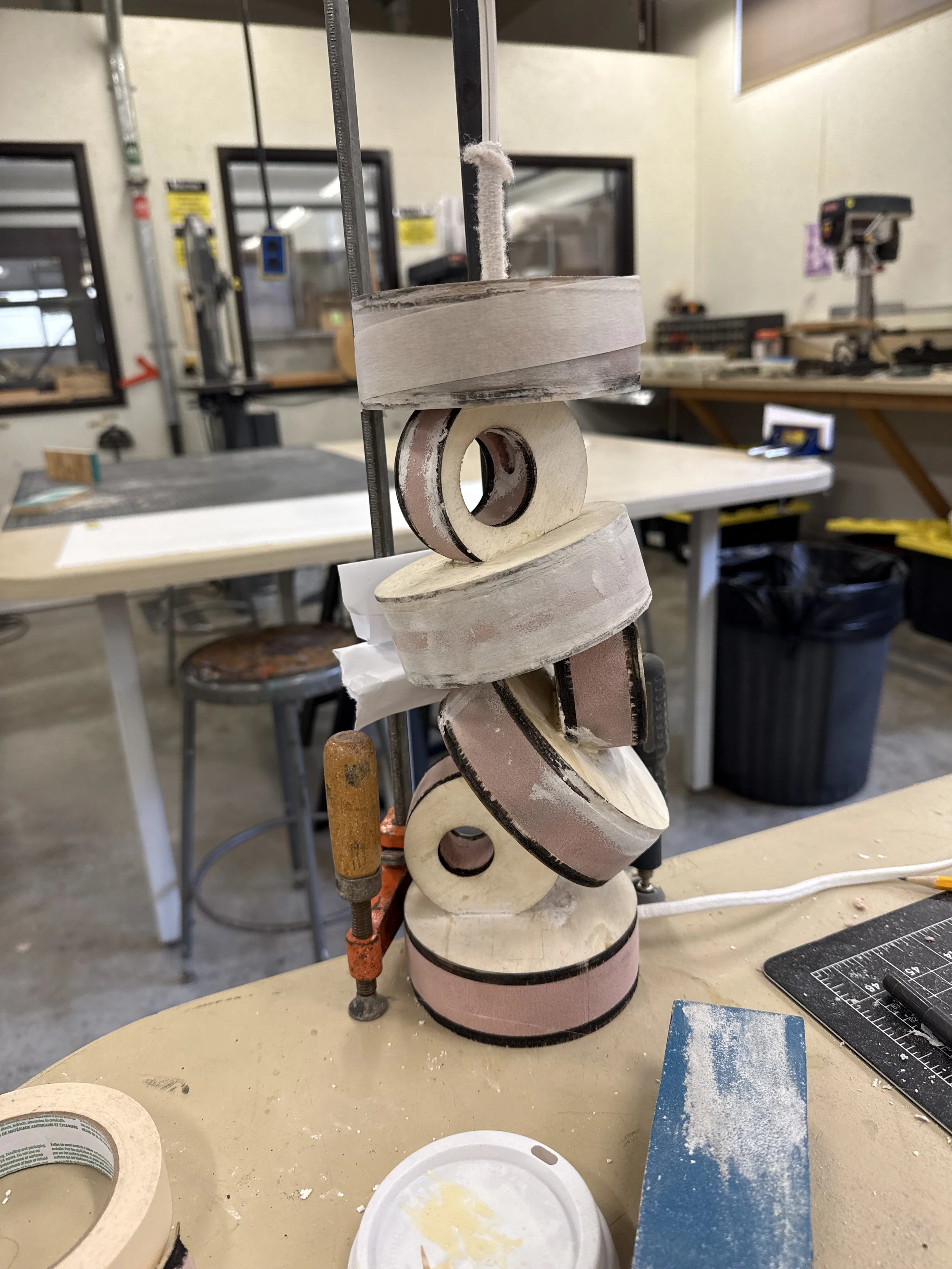 Stack of pink and black sanding pads with a wire clamp in a workshop.