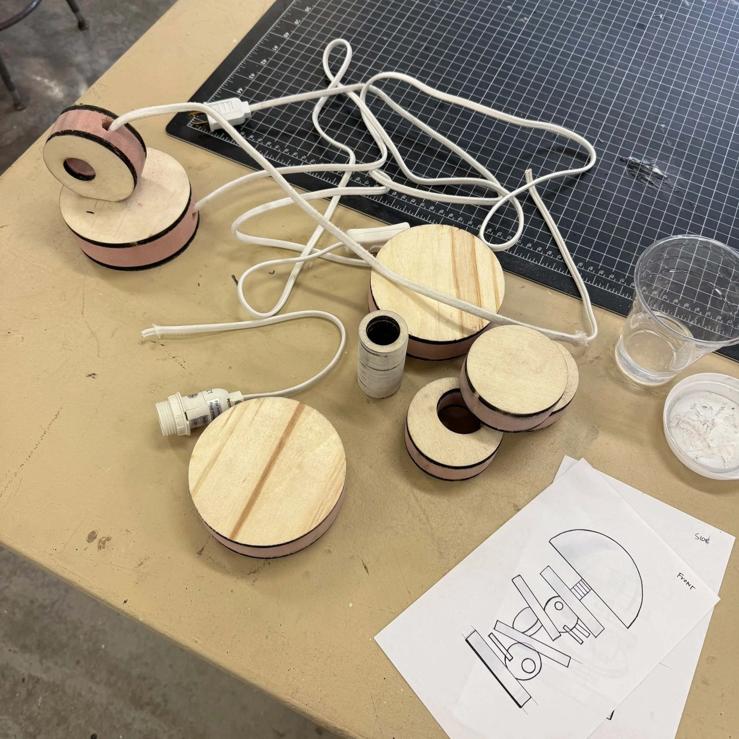 A workspace with wooden roll shapes, some white electrical cords, a black cutting mat, and architectural or engineering drawings.