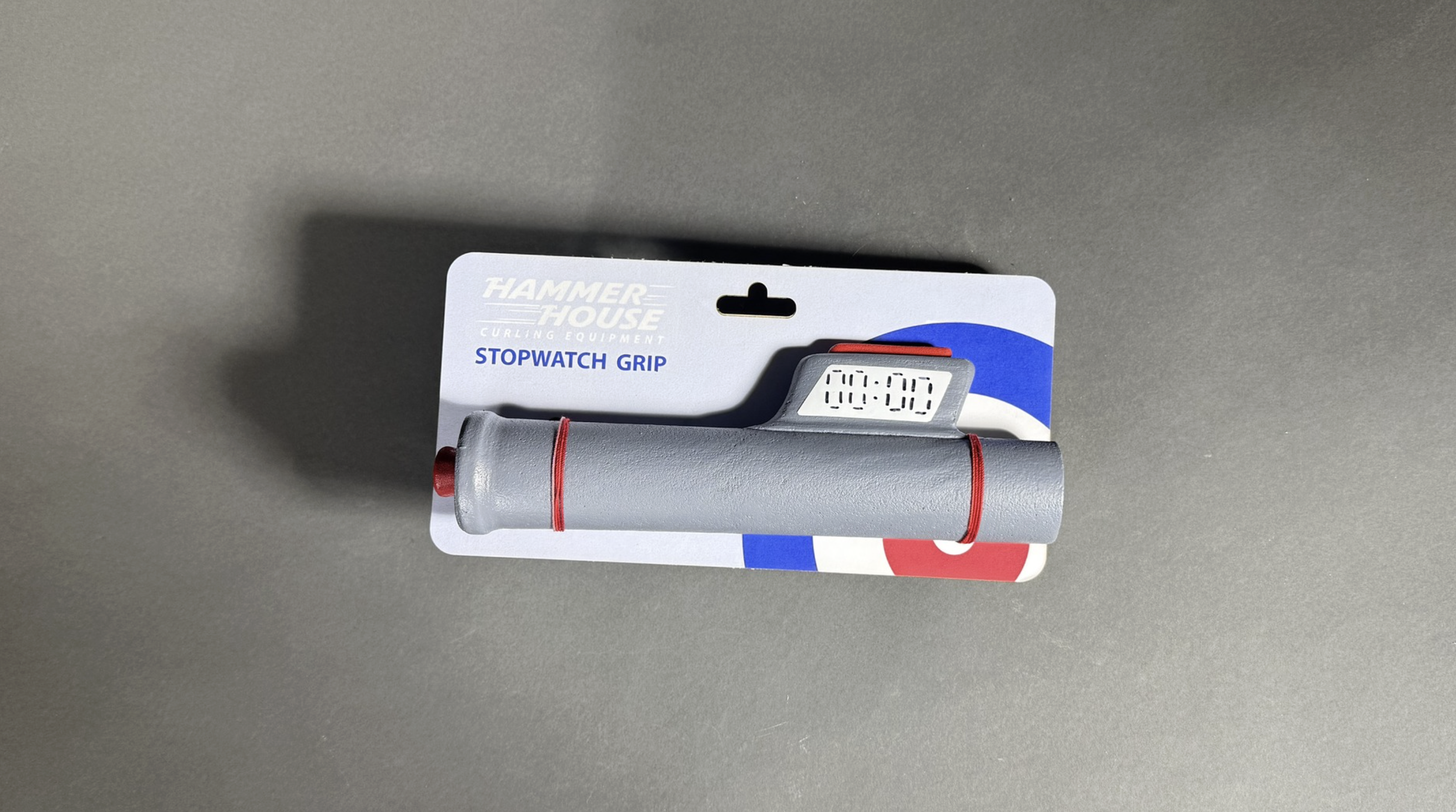 A digital stopwatch grip by Hammer House Curling Equipment, attached to its packaging, resting on a gray surface.