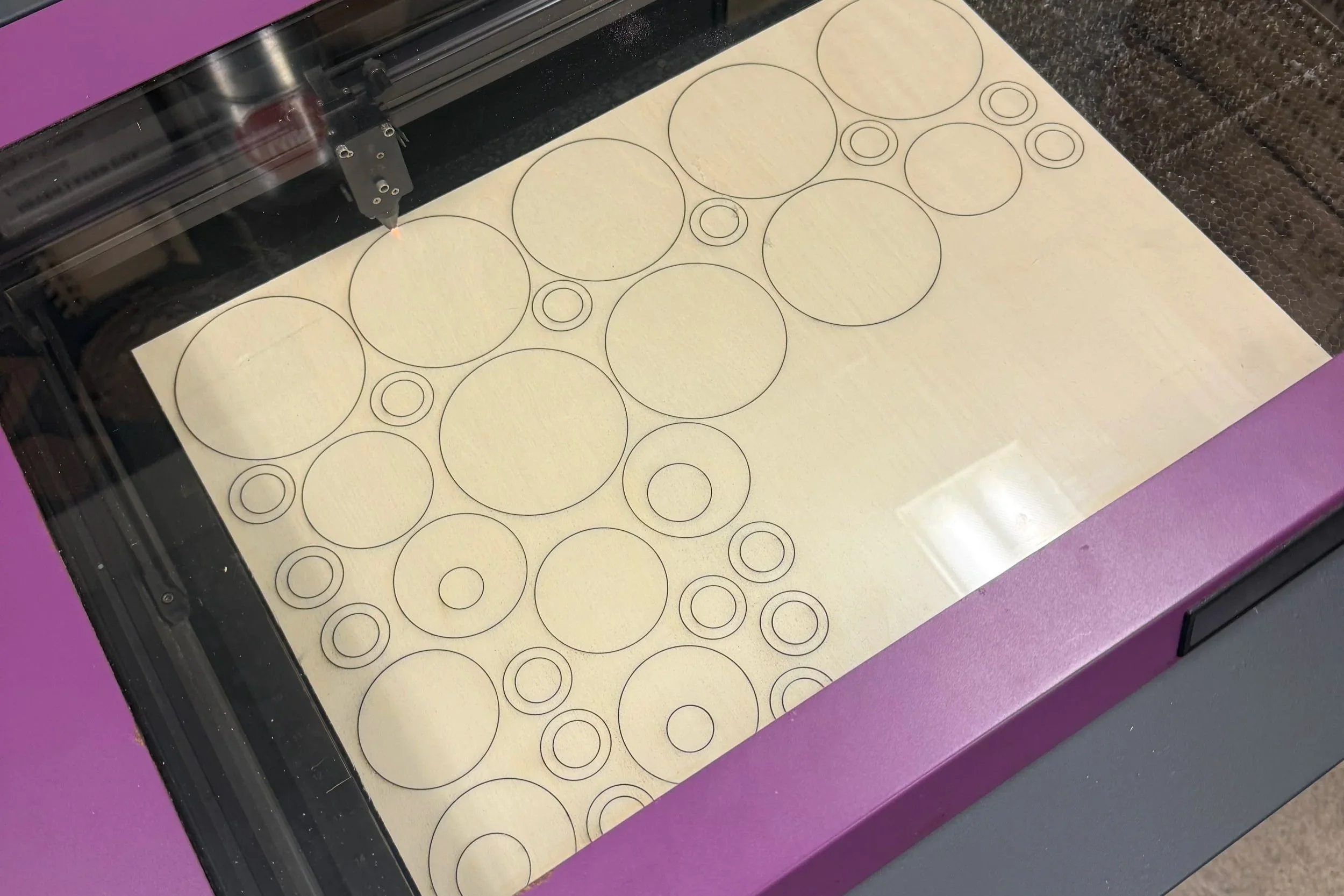 Laser cutter etching circles on a piece of wood.