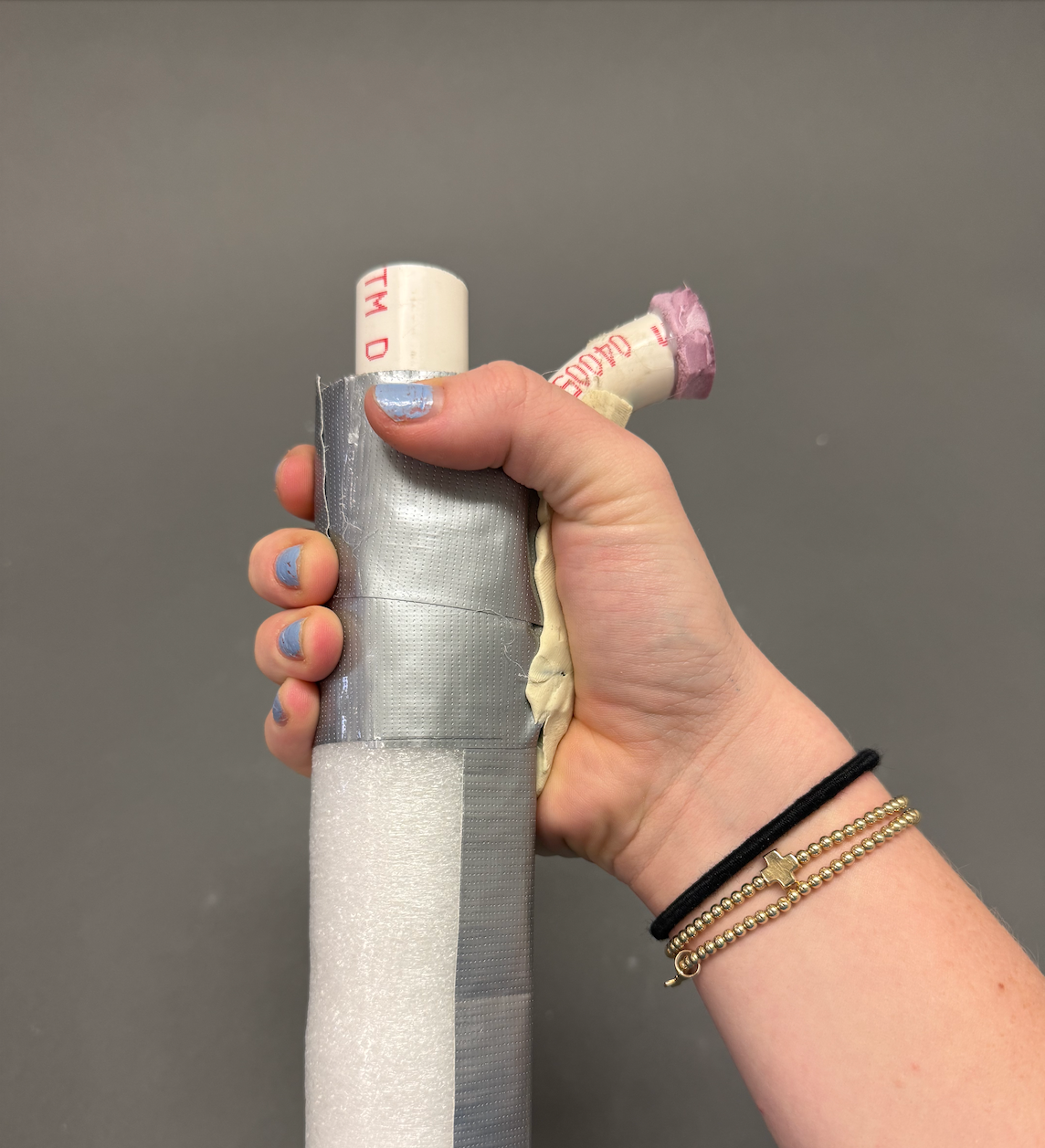 A person's hand gripping a cylindrical object wrapped in duct tape and medical tape, with two rolled pieces of medical tape protruding from the top.