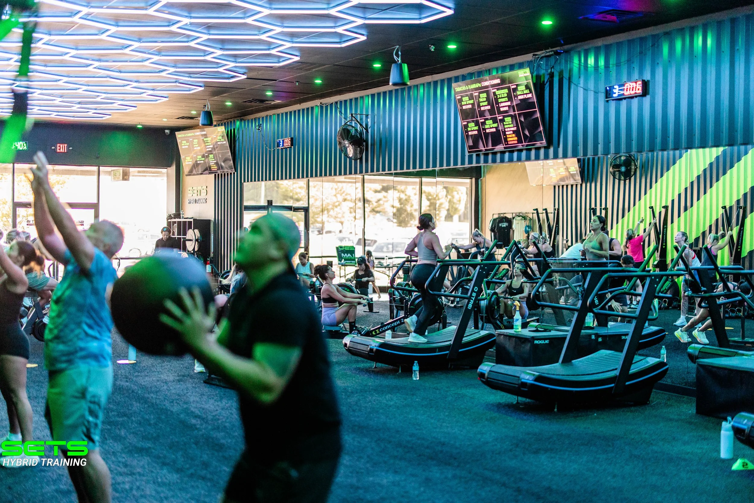 People working out on exercise machines in a modern gym with LED lights and digital screens.
