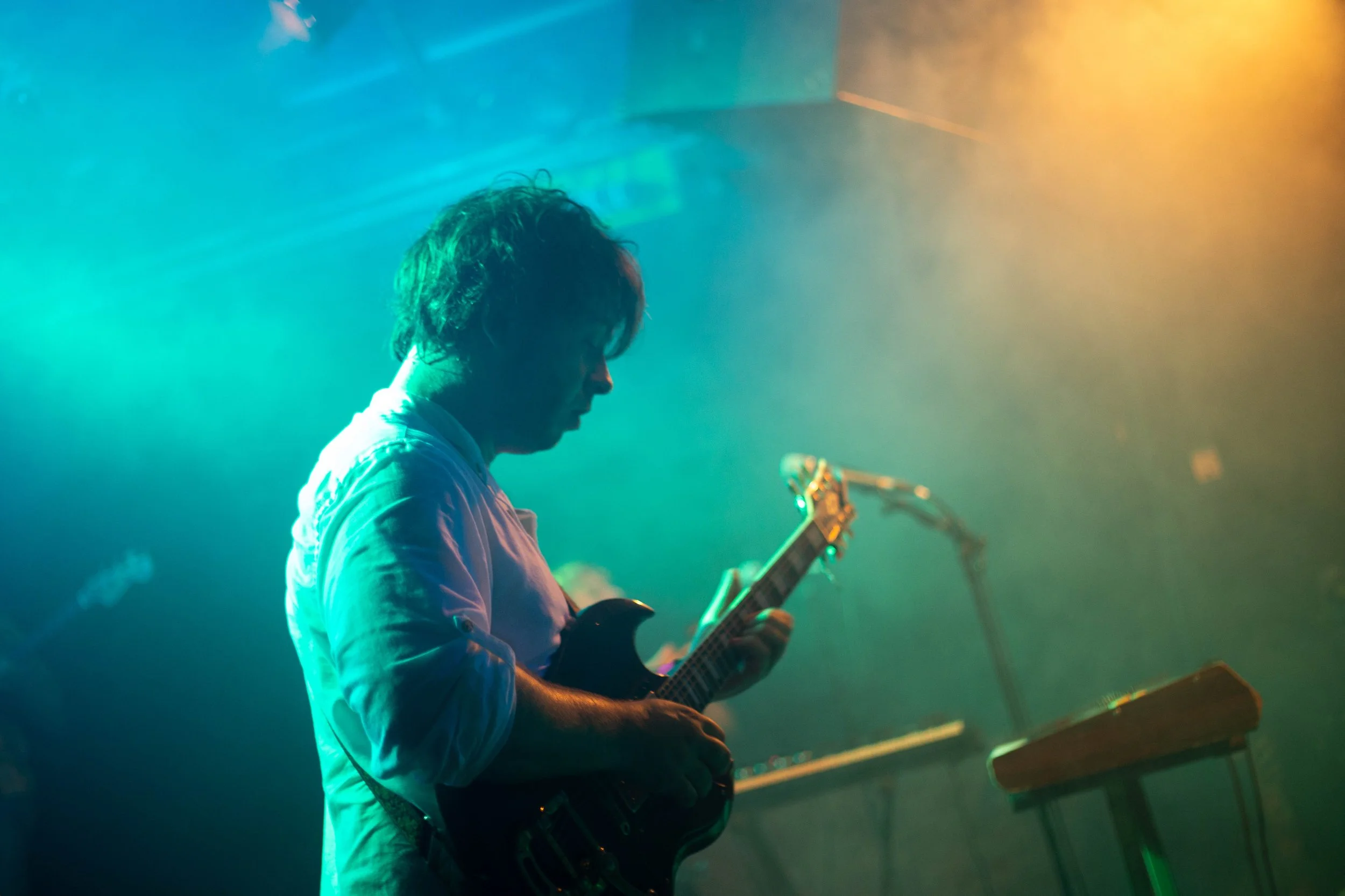 Ein Musiker spielt Gitarre in einem dunklen Raum mit bunten Lichtschein.
