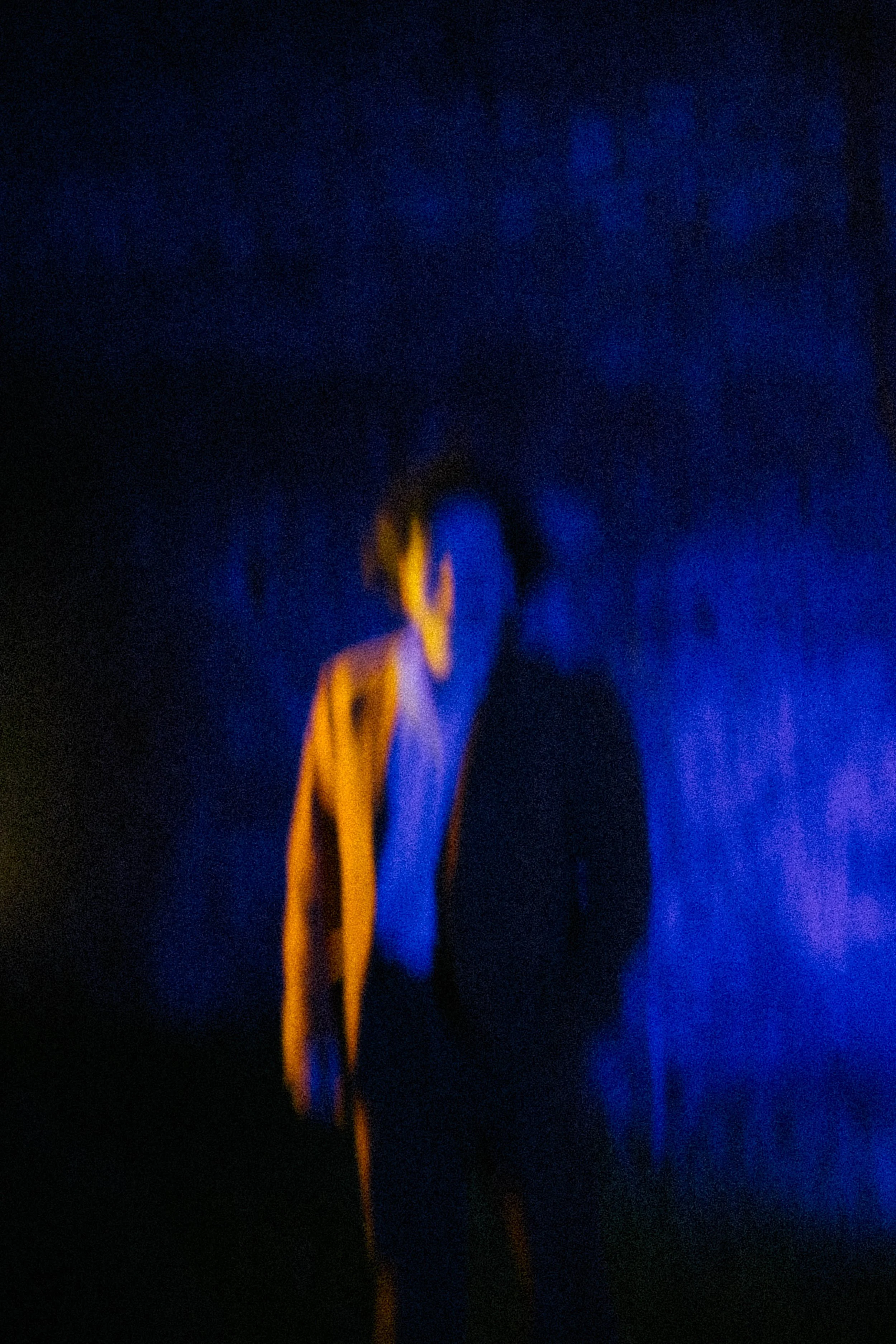 Das Bild zeigt eine dunkle Szene mit blauen und orangefarbenen Lichtern, die unklare Formen und Linien bilden.