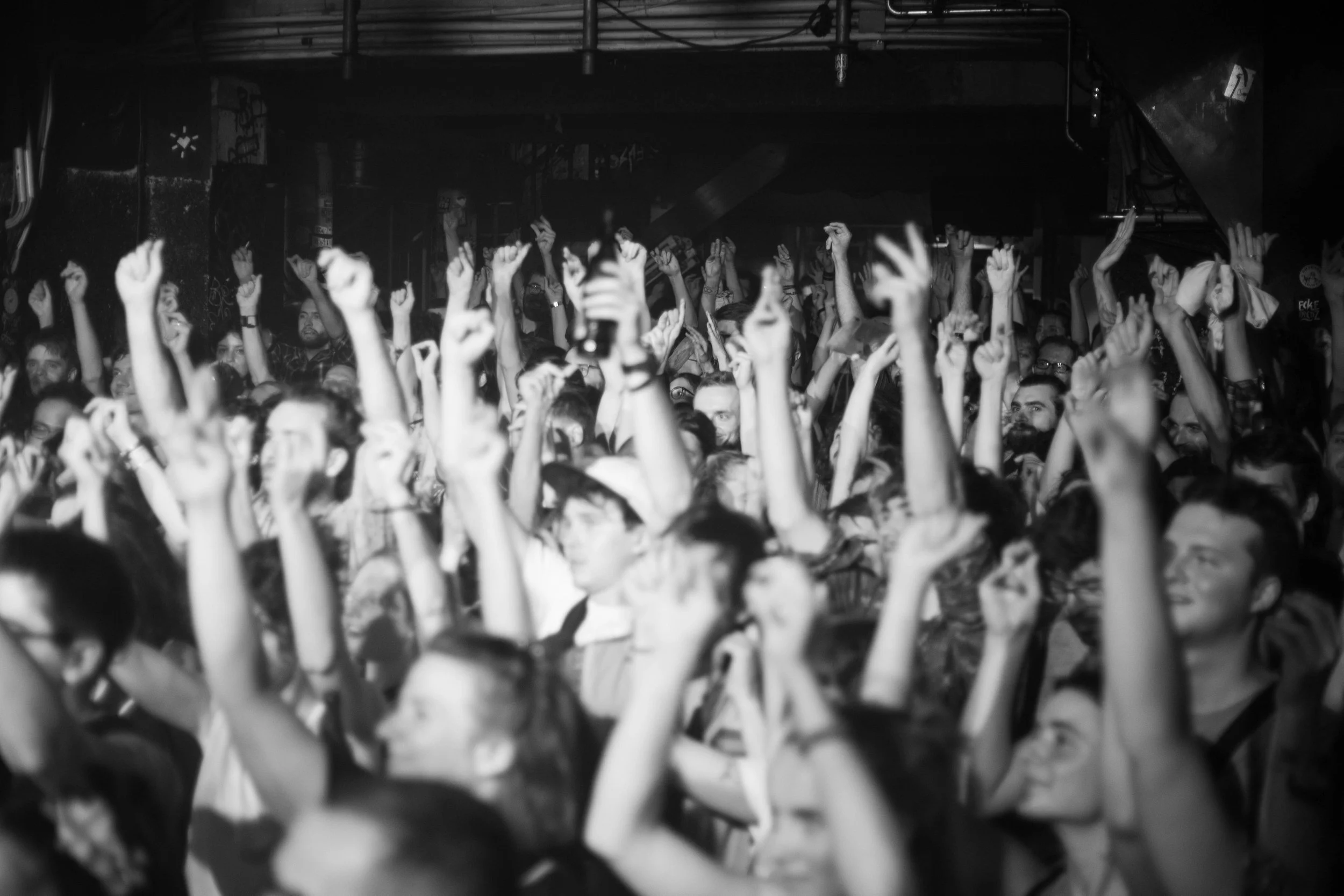 Menschen in einer dunklen Club- oder Konzertumgebung, die mit erhobenen Armen tanzen.