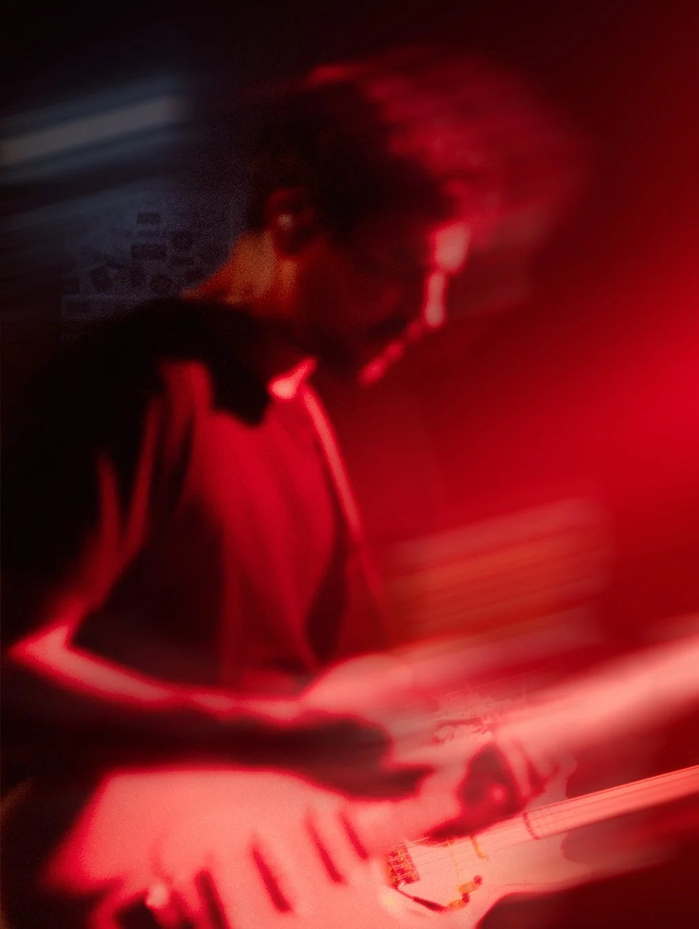 Eine Person mit dunklen Haaren und Brille spielt E-Gitarre in einem dunklen Raum mit rotem Licht.