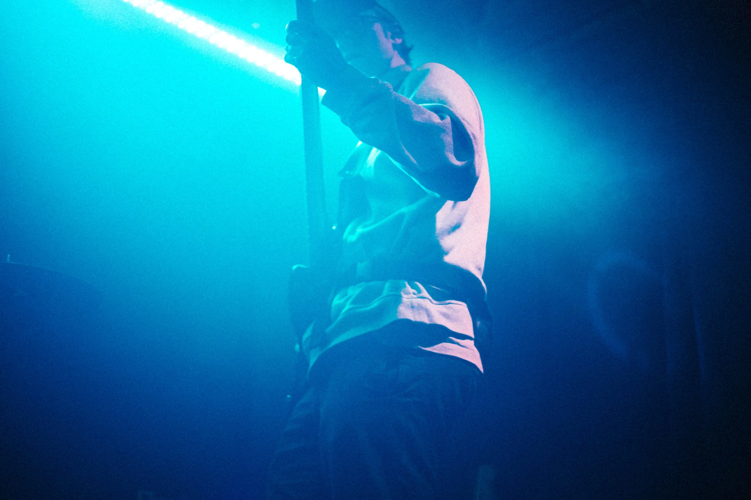 Junge Person in Jeans und Hoodie in dunklem Raum mit blauer Lichtquelle