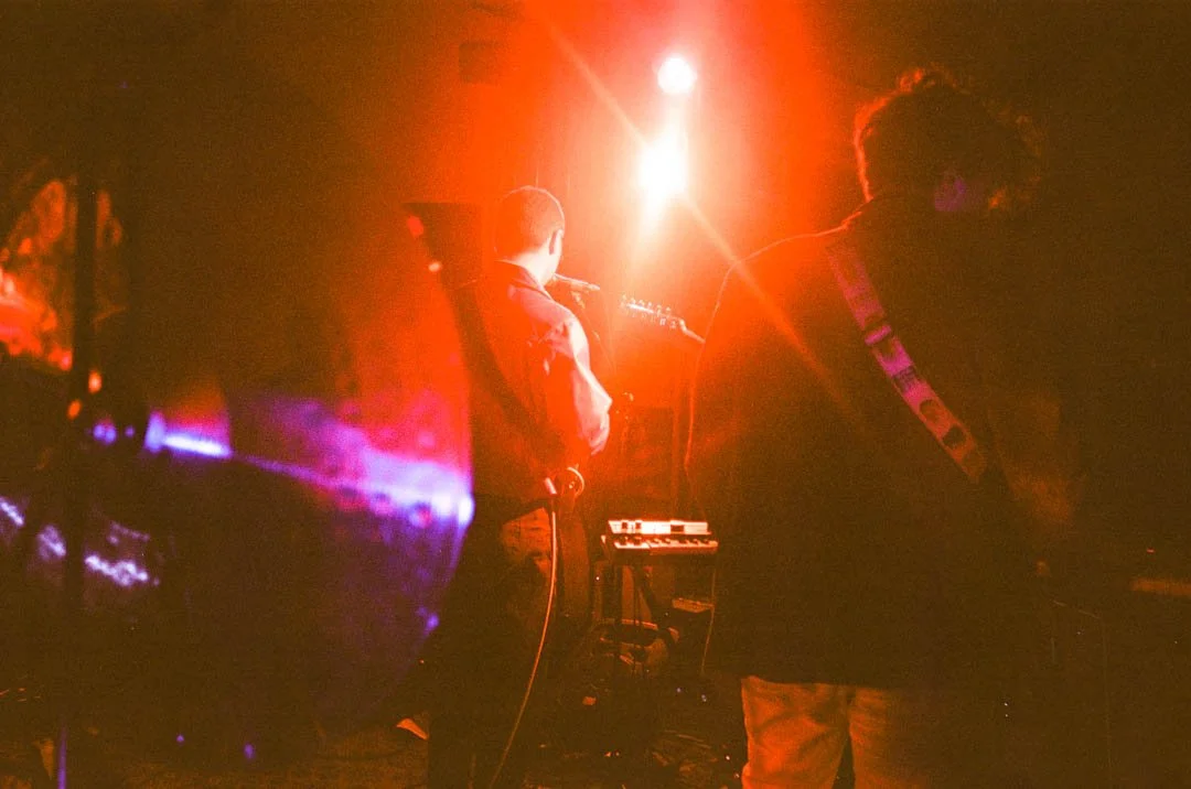 Musiker und Musikerin spielen auf einer Bühne bei rotem Licht, mit einem Keyboard und Gitarren, live. nachts, dunkle Umgebung.