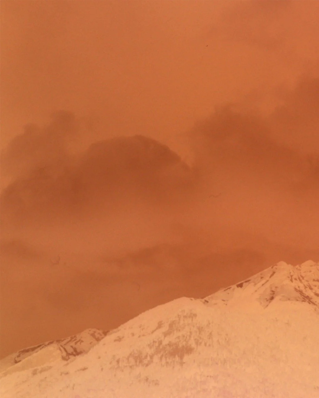 Verschneite Berge unter einem orangefarbenen Himmel mit dunklen Wolken.