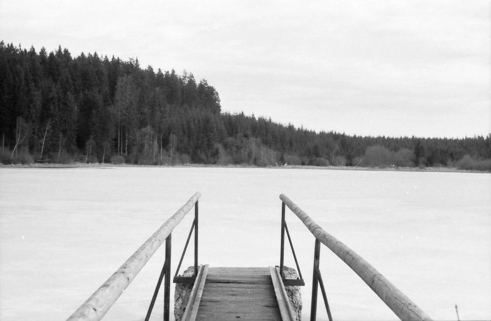 Schneebedeckter See mit Holzsteg und Baumwald im Hintergrund