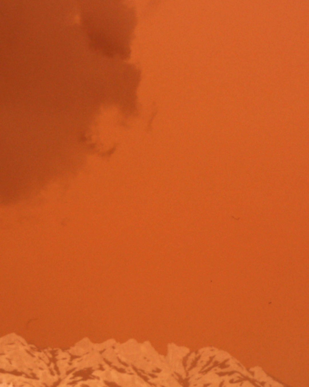 Berggipfel mit schneebedeckten Bergen im Vordergrund, orangefarbenes Himmel mit dunklen Wolken
