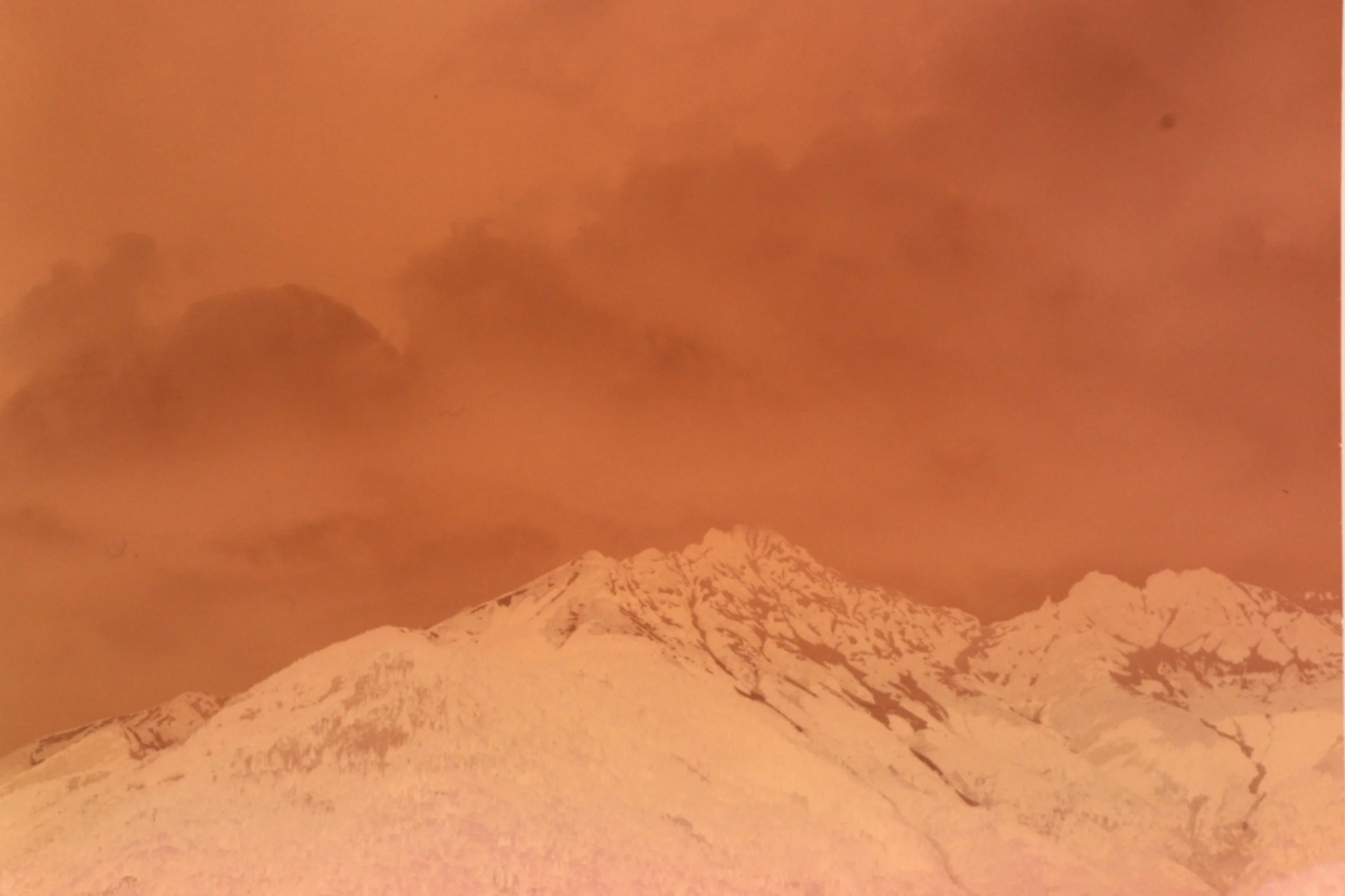 Schneebedeckter Berg unter orangefarbenem Himmel mit Wolken