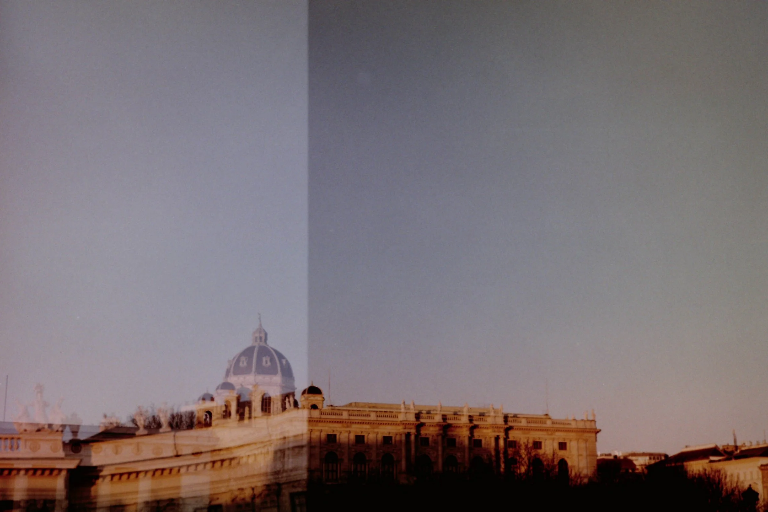 Ein Stadtbild mit einem historischen Gebäude, das eine große Kuppel hat, bei Sonnenuntergang, teilweise durch eine Überblendungseffekt geteilt.