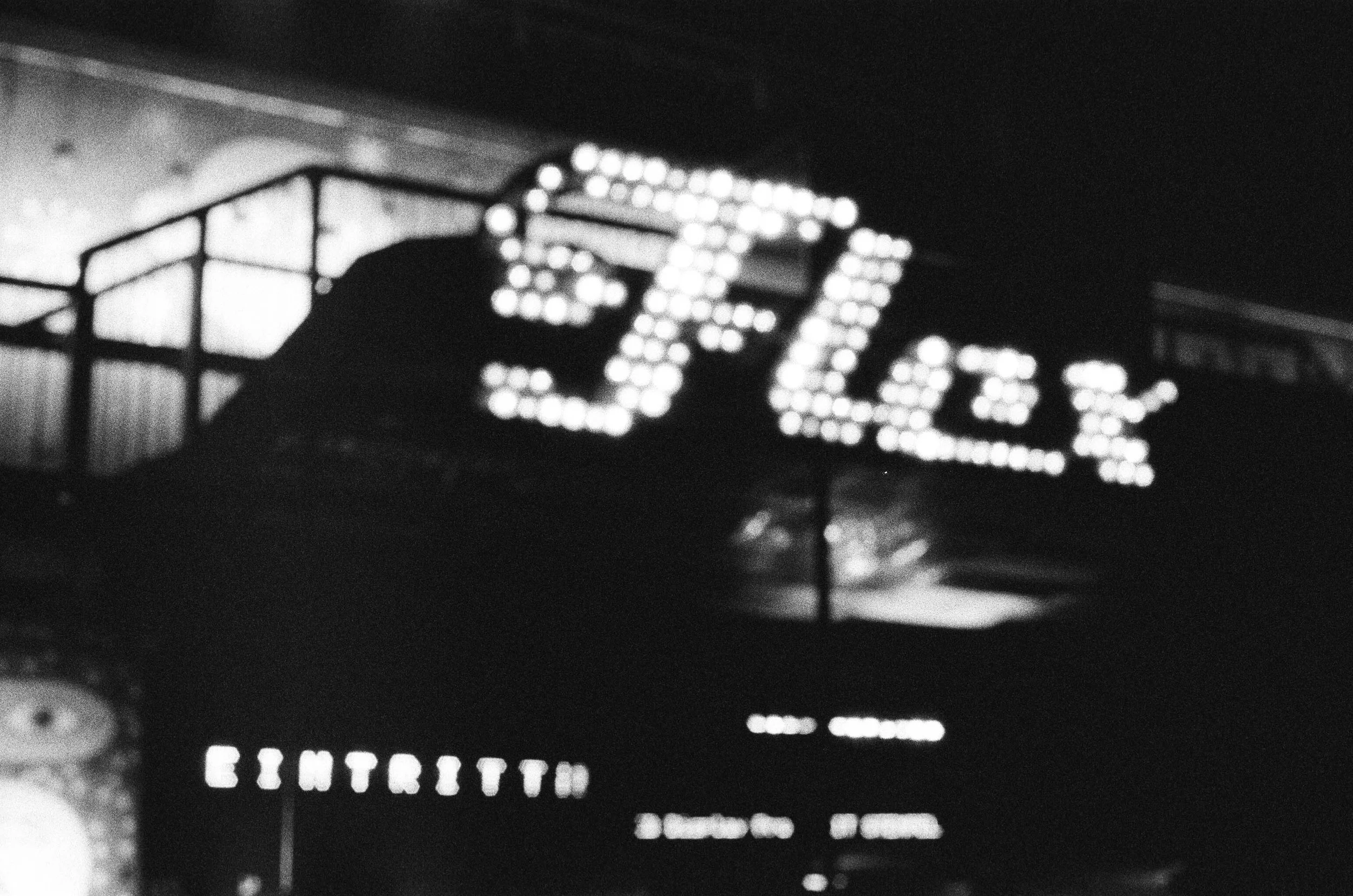Ein schwarzes und weißes Bild eines digitalen Schildes mit leuchtenden Punkten, das die Zahl 60 zeigt, und darunter die Worte 'ENTRANCE'.
