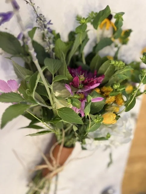Bouquet of mixed wildflowers with green leaves, pink, yellow, purple, and white flowers, tied with a string.