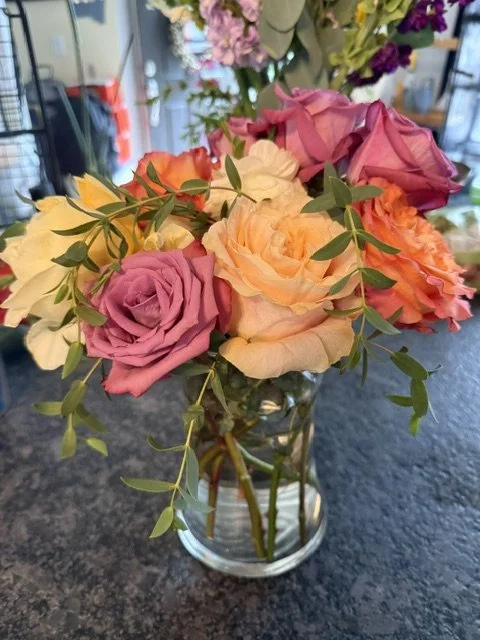 A bouquet of colorful roses in a glass jar on a dark countertop.
