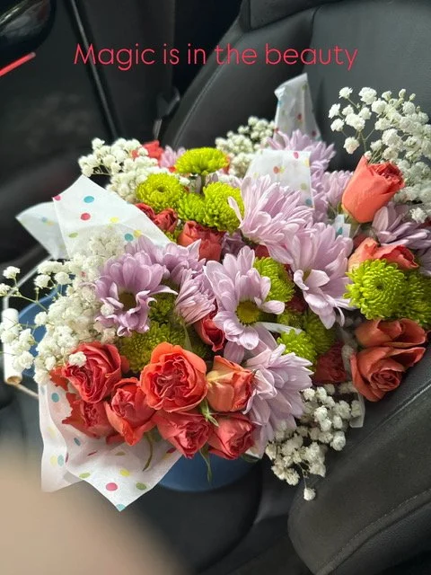 A bouquet of colorful flowers, including roses, chrysanthemums, and baby's breath, with a pink text overlay that says "Magic is in the beauty".