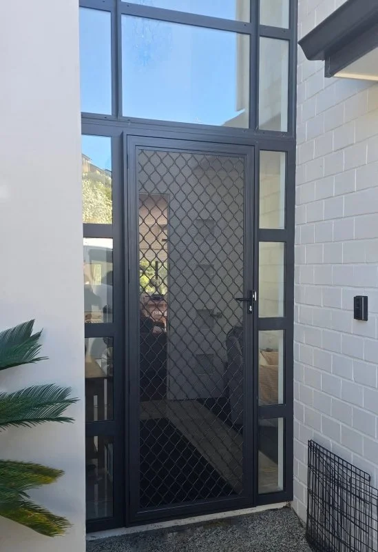Modern black security screen door with diamond-pattern mesh and glass sidelights at a contemporary home entrance